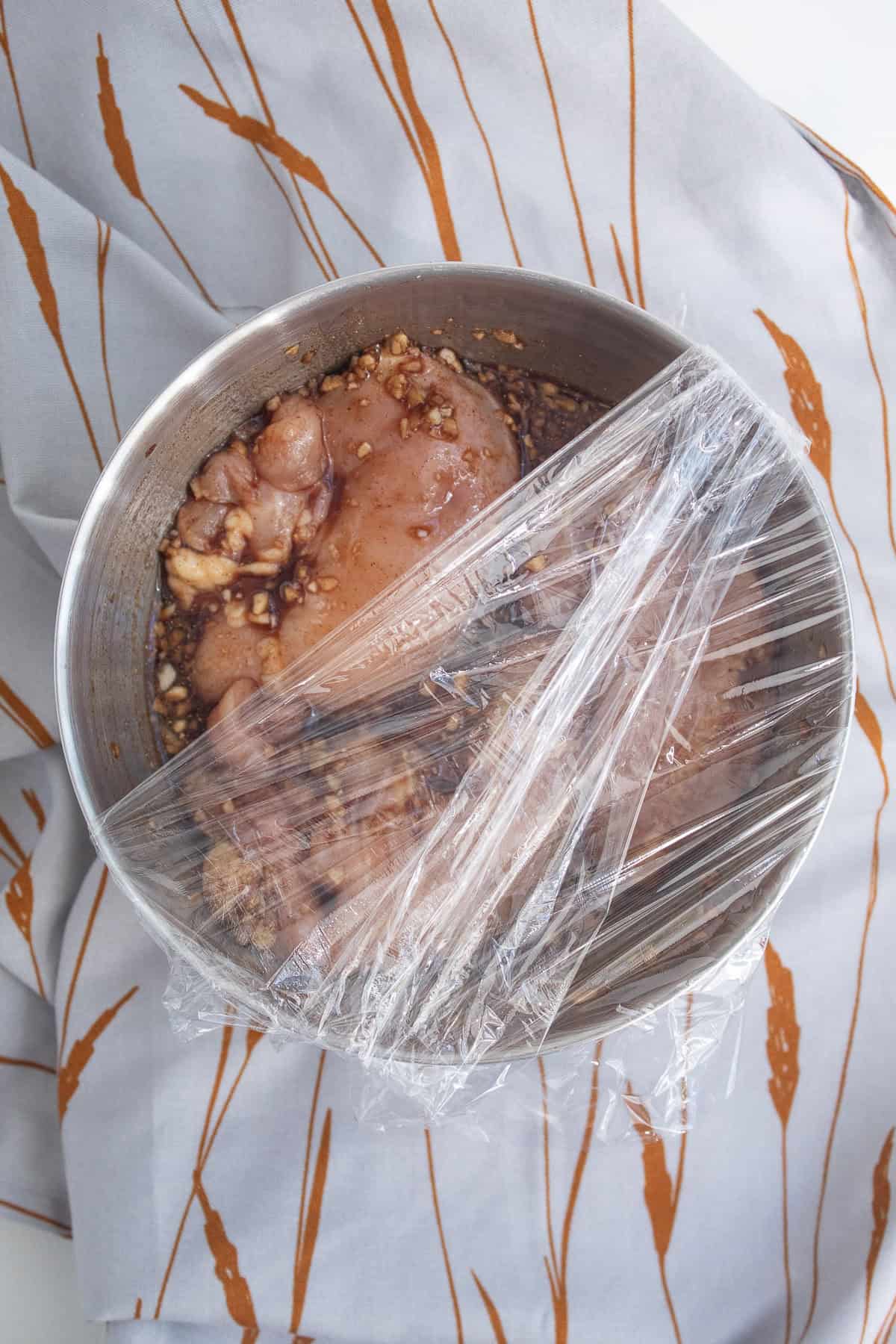 The marinating chicken thighs are covered with plastic wrap.