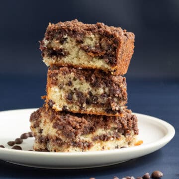A stack of three slices of coffee cake freckled with chocolate chips and streusel sits on a white plate.