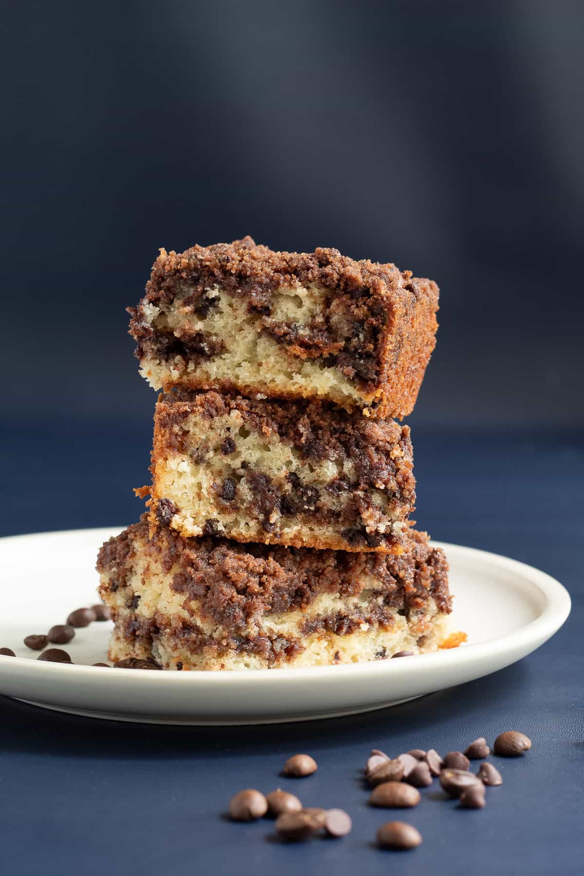 A stack of three slices of coffee cake freckled with chocolate chips and streusel sits on a white plate.