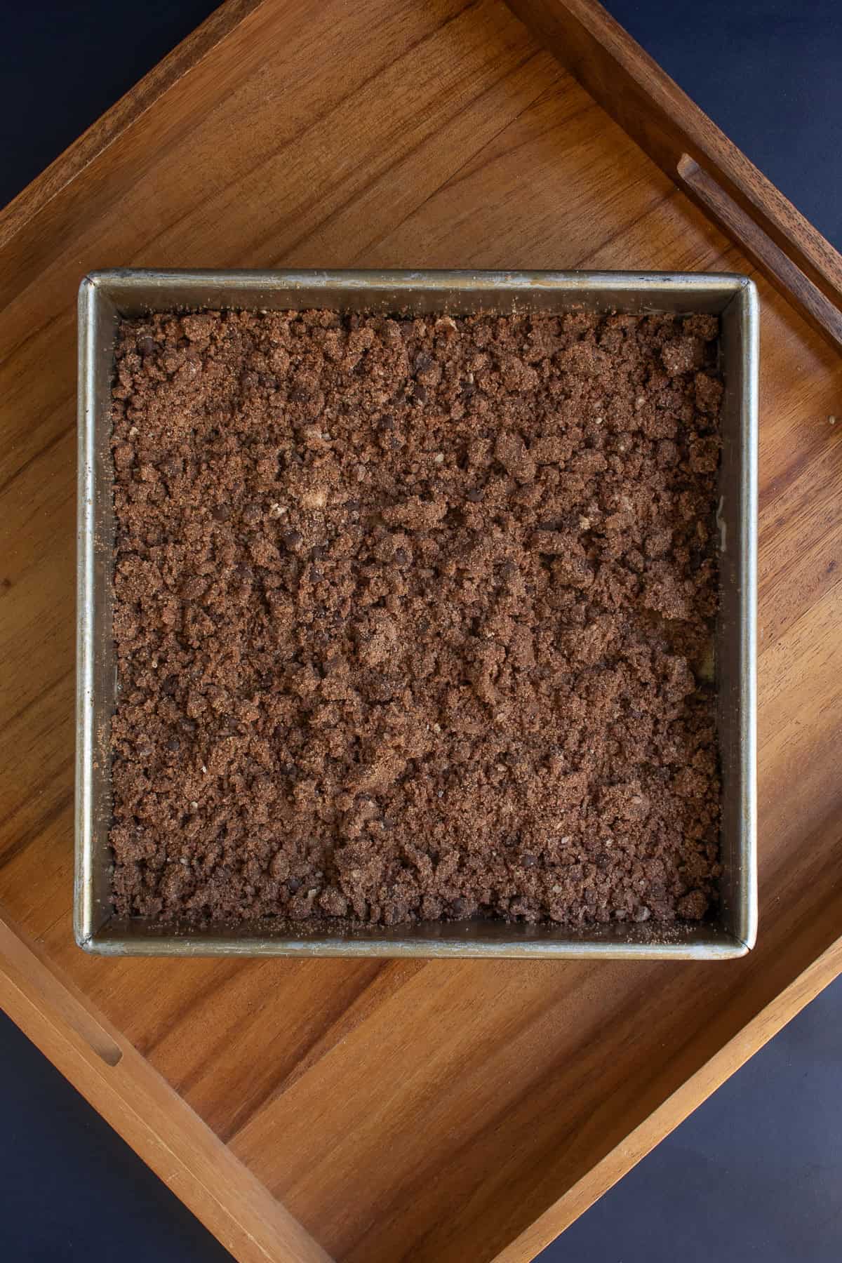 Brown streusel topping is sprinkled over the wet batter in the square pan.