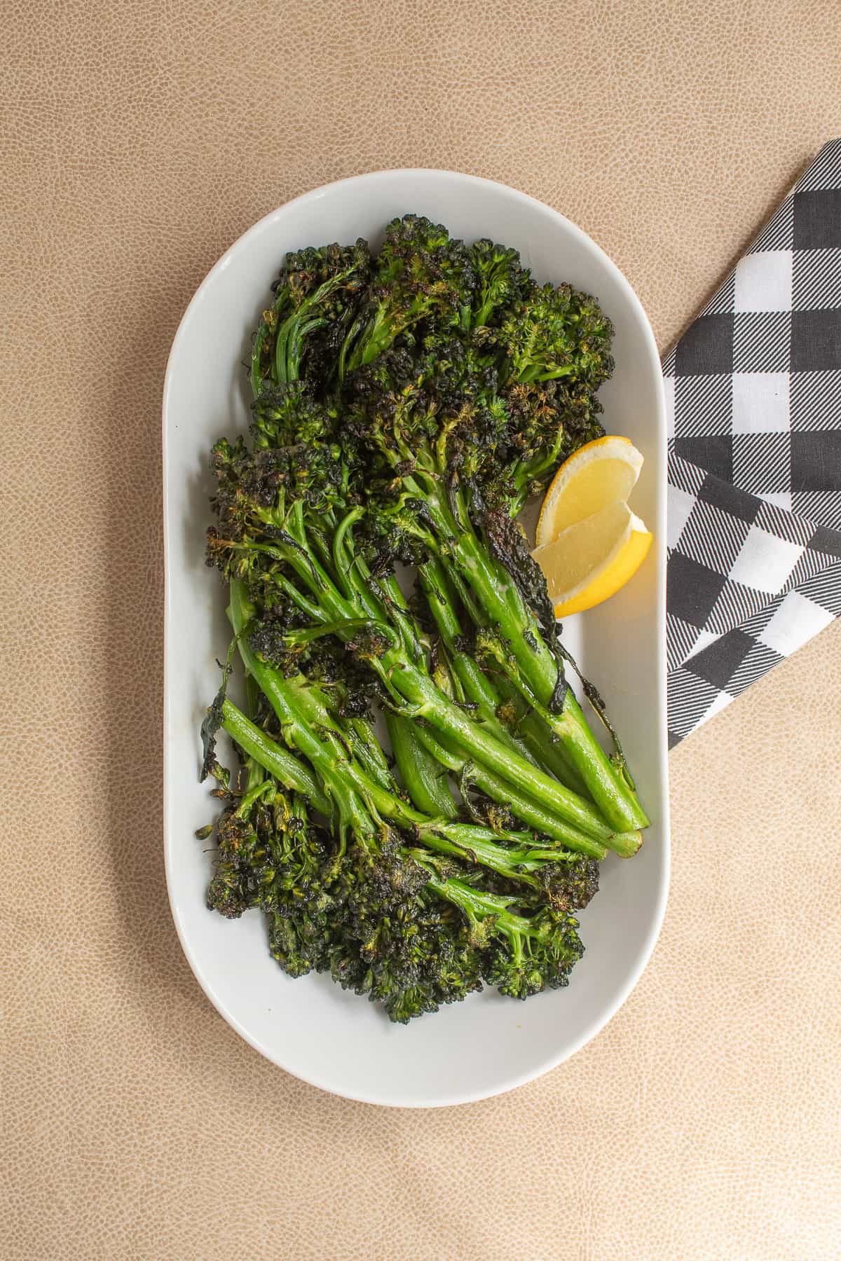 Tender green stalks of broccolini with crisp florets are piled into a serving platter with lemon wedges for garnish.