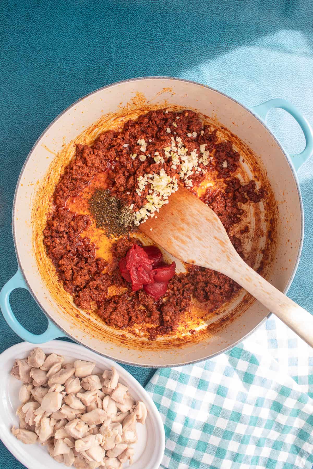 Tomato paste, oregano, and diced garlic are added to the browned chorizo in the pot.