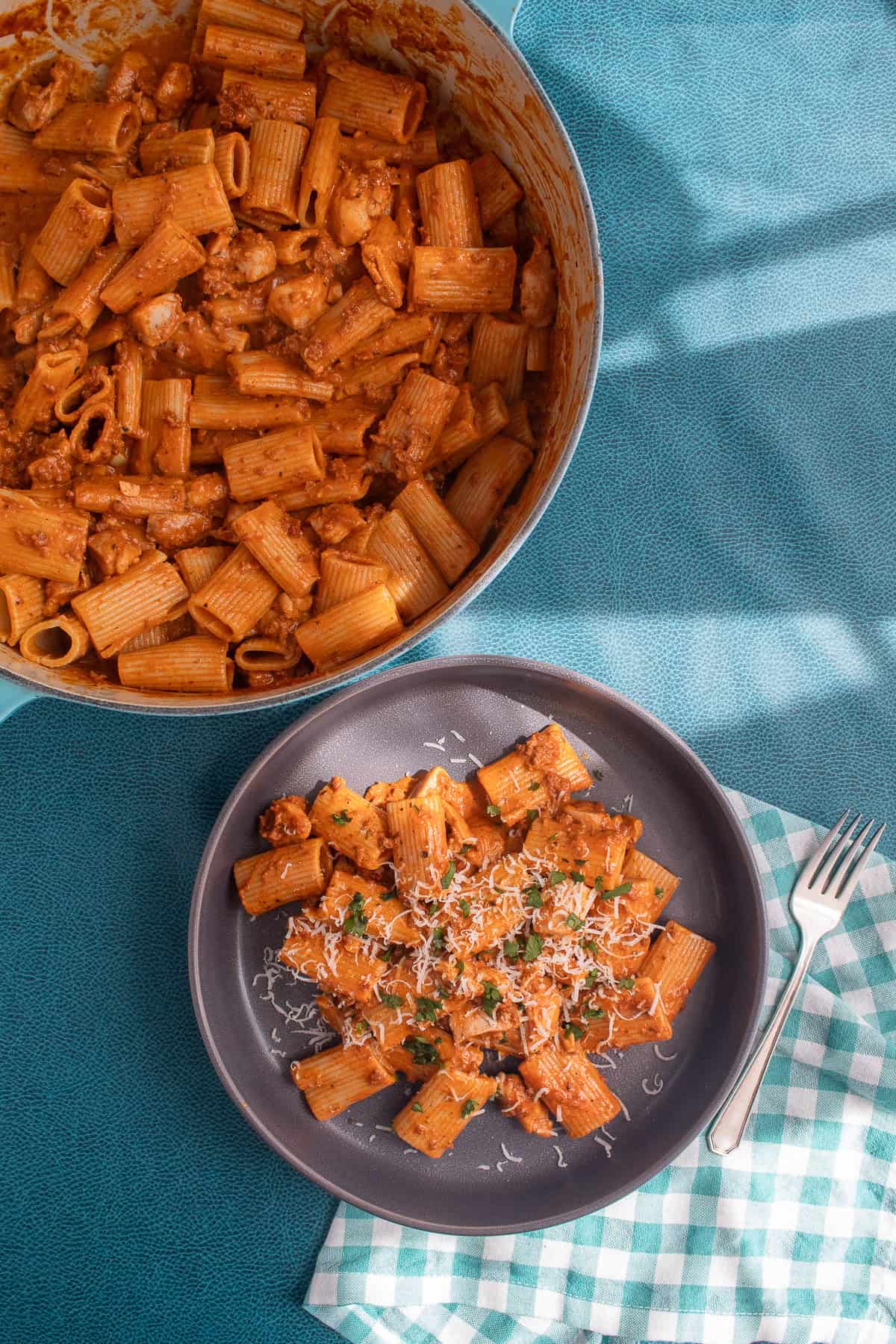 A garnished serving of the pasta dish on a gray plate next to a pot of the finished pasta.