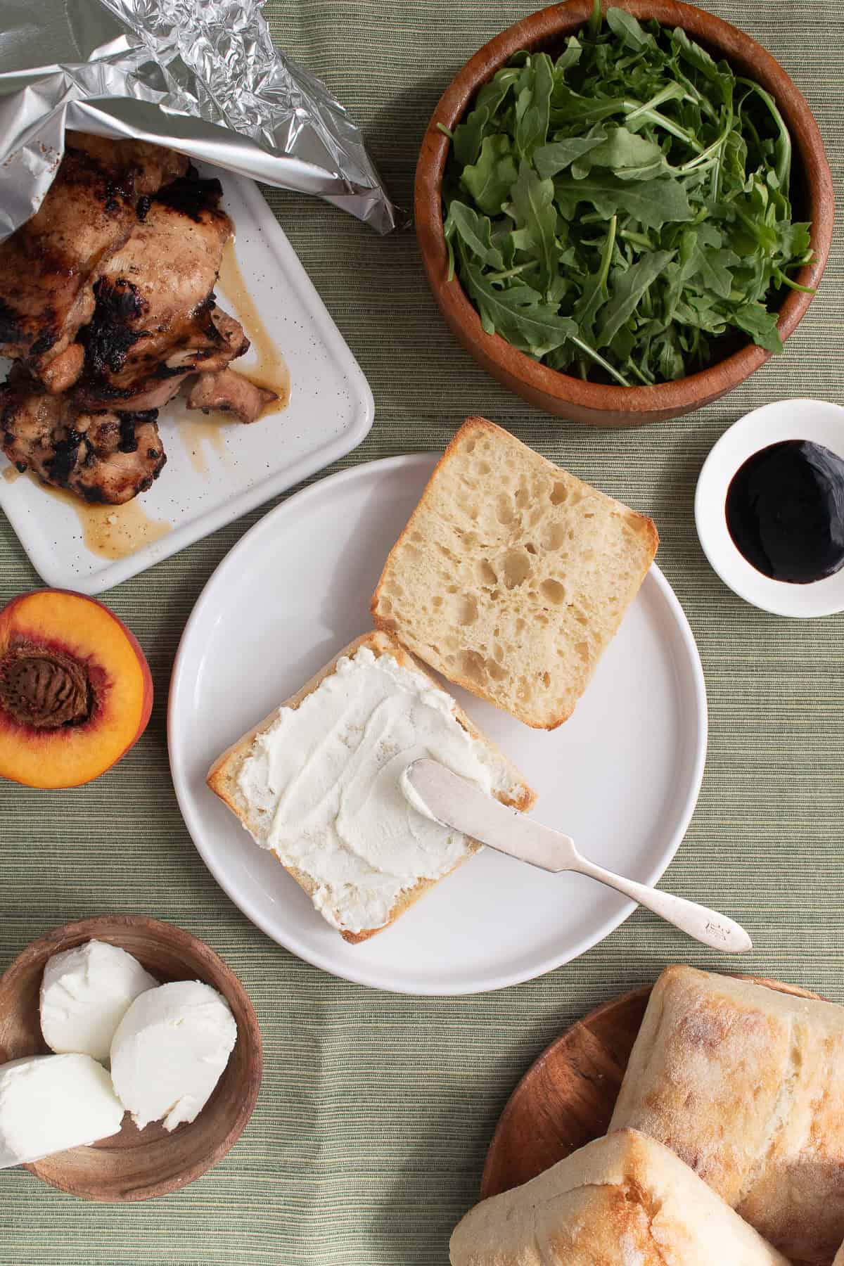 Goat cheese is spread over half of a ciabatta bun.