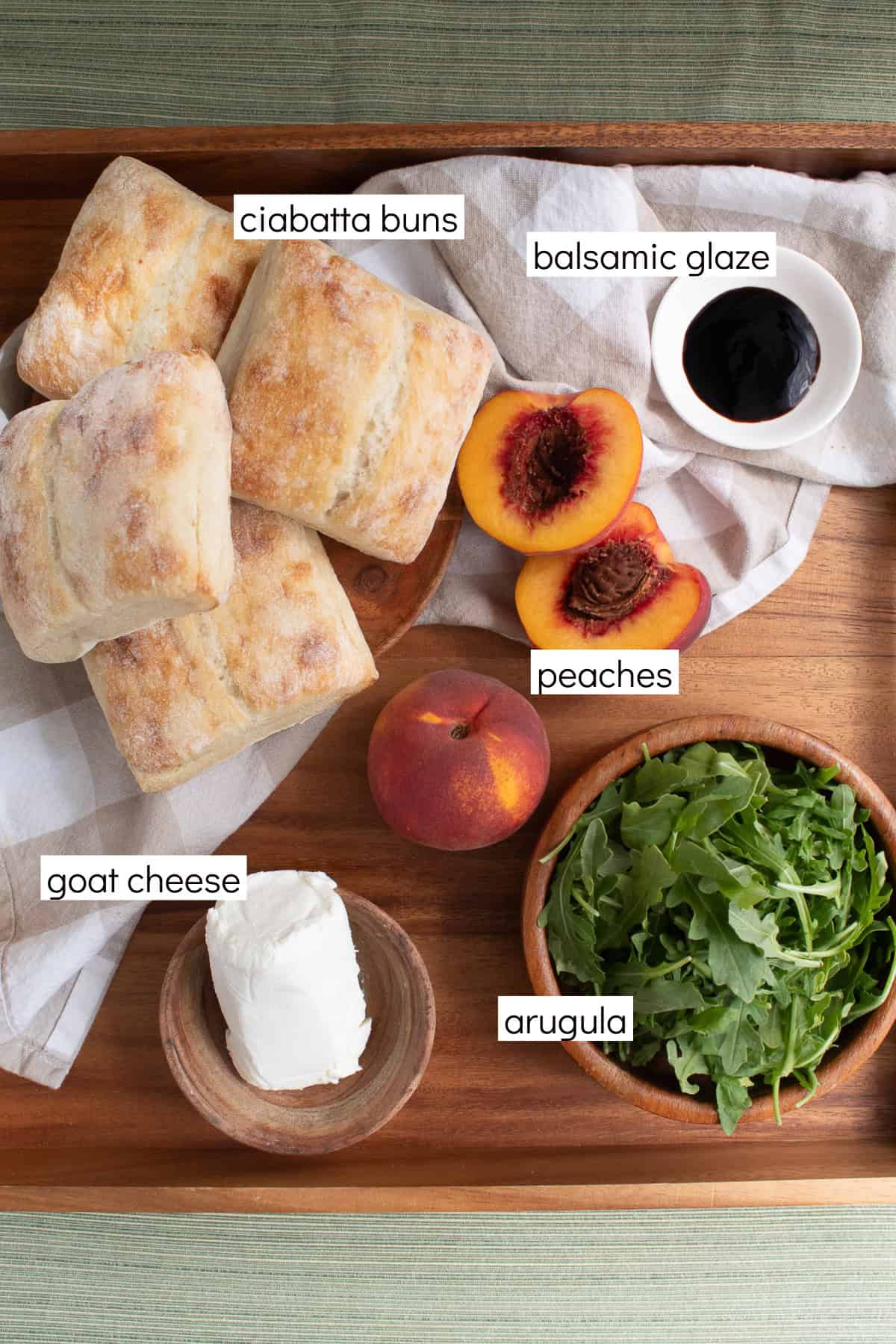 Ingredients for the sandwiches are displayed and labeled with white text boxes including the words ciabatta buns, balsamic glaze, peaches, goat cheese, and arugula.