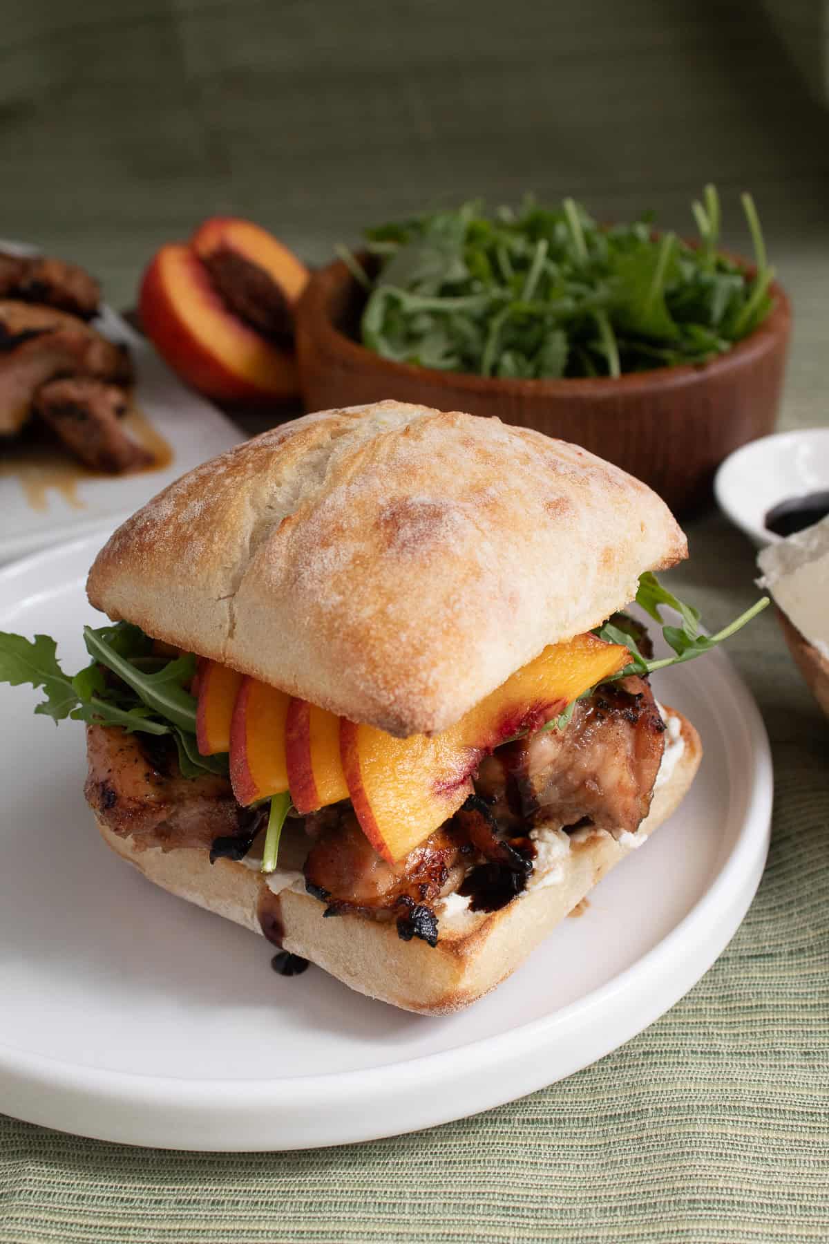 The chicken and peach sandwich with grilled chicken thigh is on a toasted ciabatta bun with arugula and goat cheese.