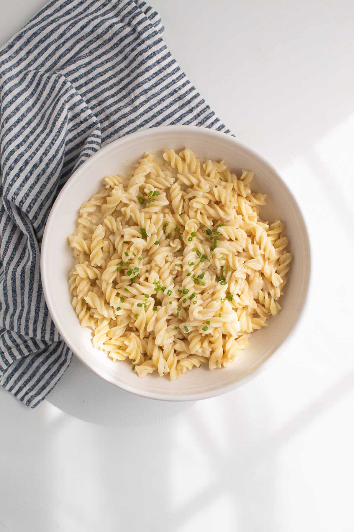 The finished creamy pasta is piled into a white bowl and garnished with chives.