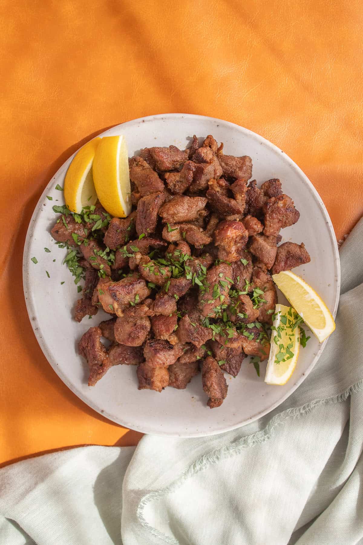 Pieces of spiced lamb are served on a platter and garnished with herbs and lemon wedges.