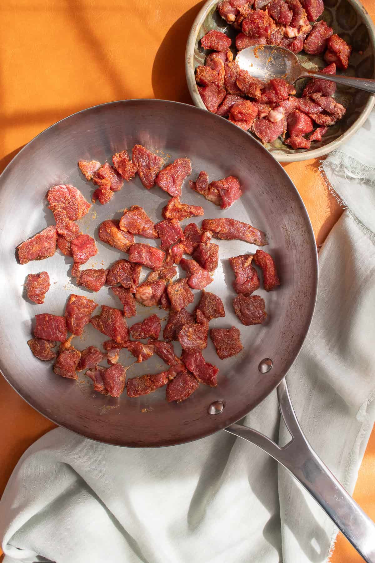 The lamb pieces are seared on a stainless steel skillet.