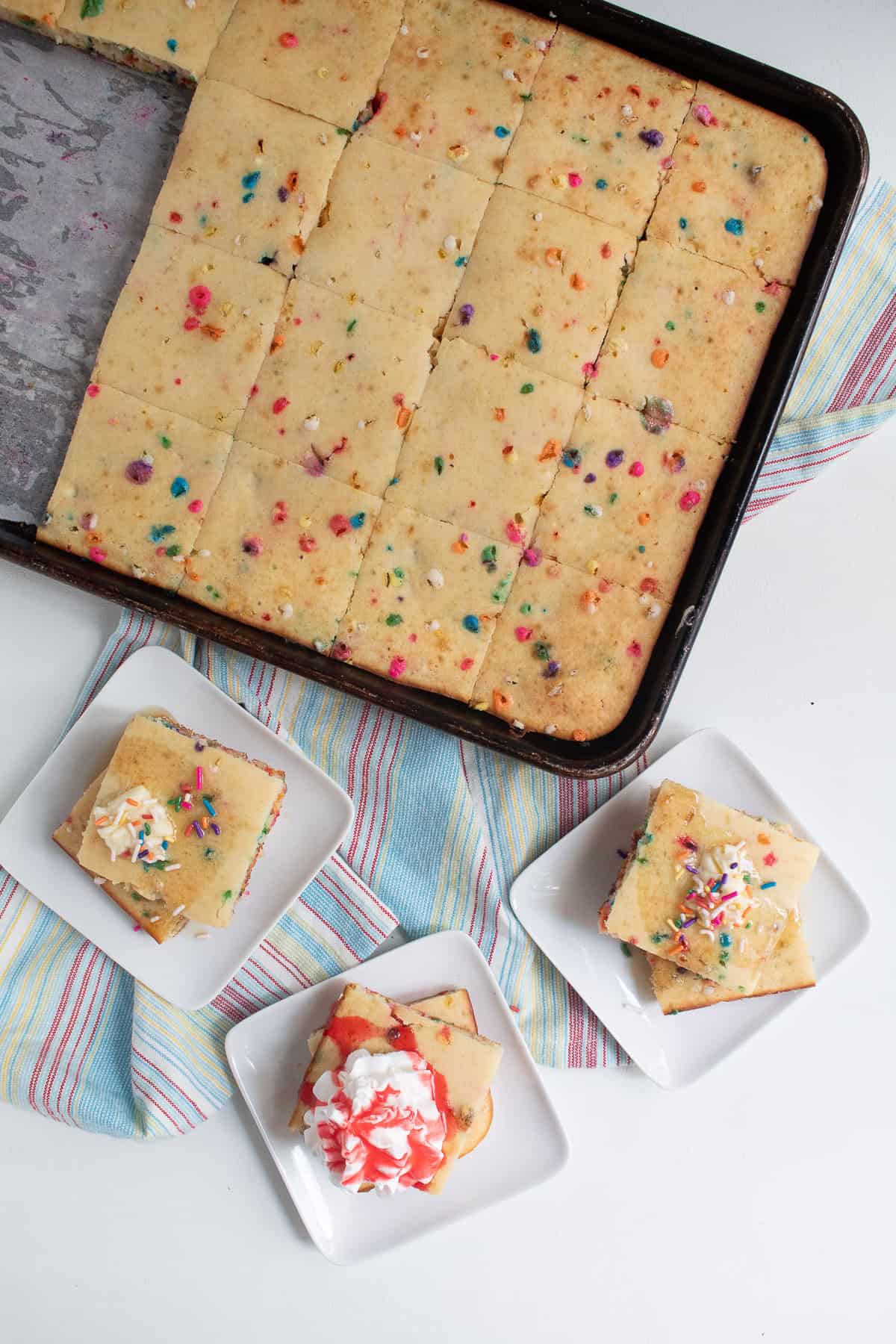 Pancakes are topped with butter, syrup, whipped cream, and strawberry syrup.