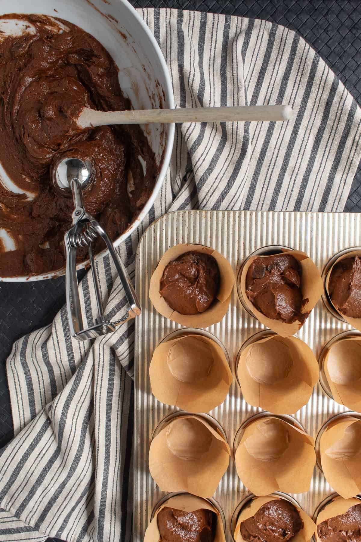 The muffin liners are filled with the batter using a scoop.