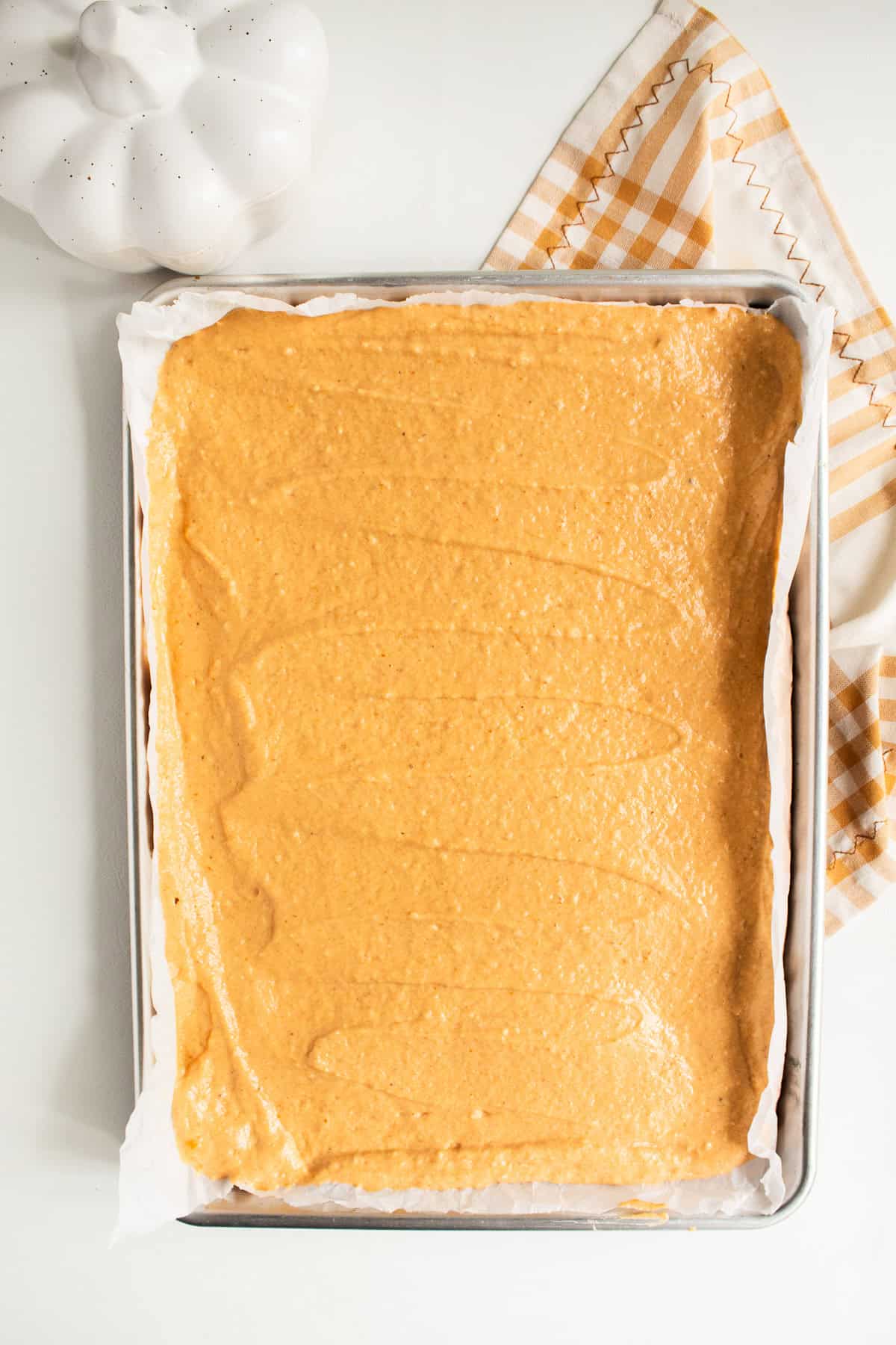 The pumpkin spice pancake batter is smoothed out over a sheet pan.