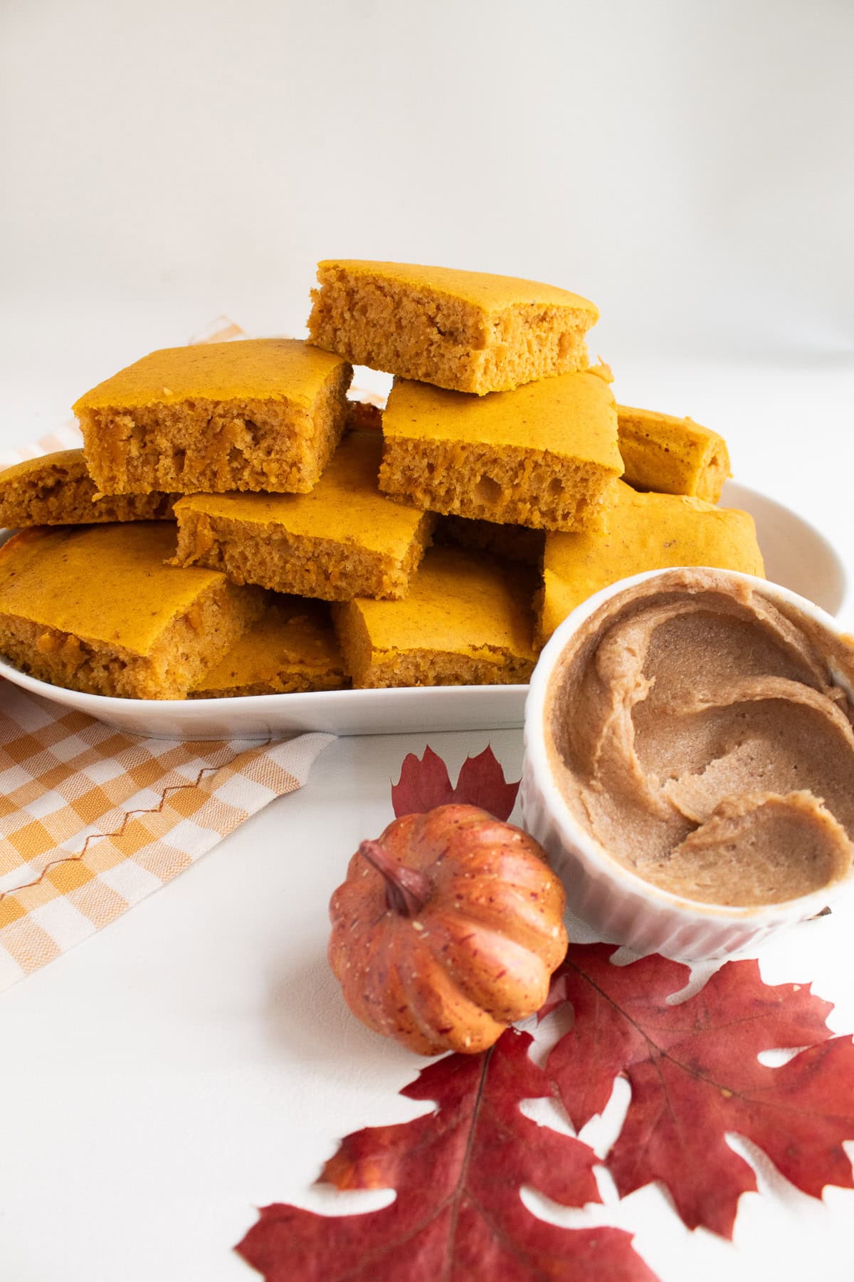 Pancakes are stacked on an oval platter next to a small bowl of whipped butter.