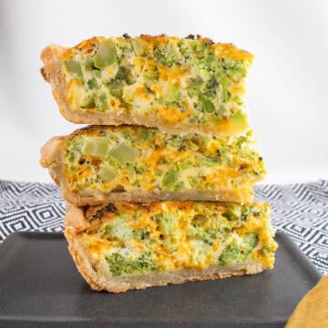 Slices of quiche are stacked and the filling is visibly full of broccoli and cheddar.