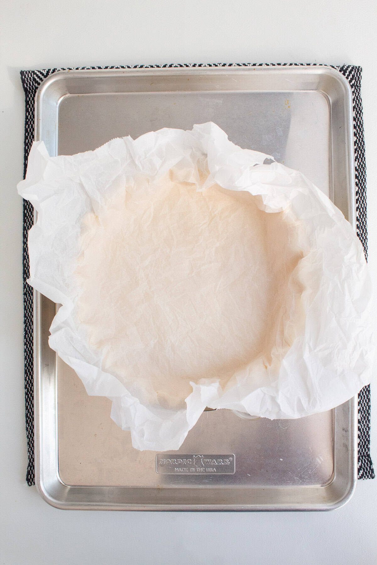 The quiche crust is lined with a piece of parchment paper before filling with pie weights.
