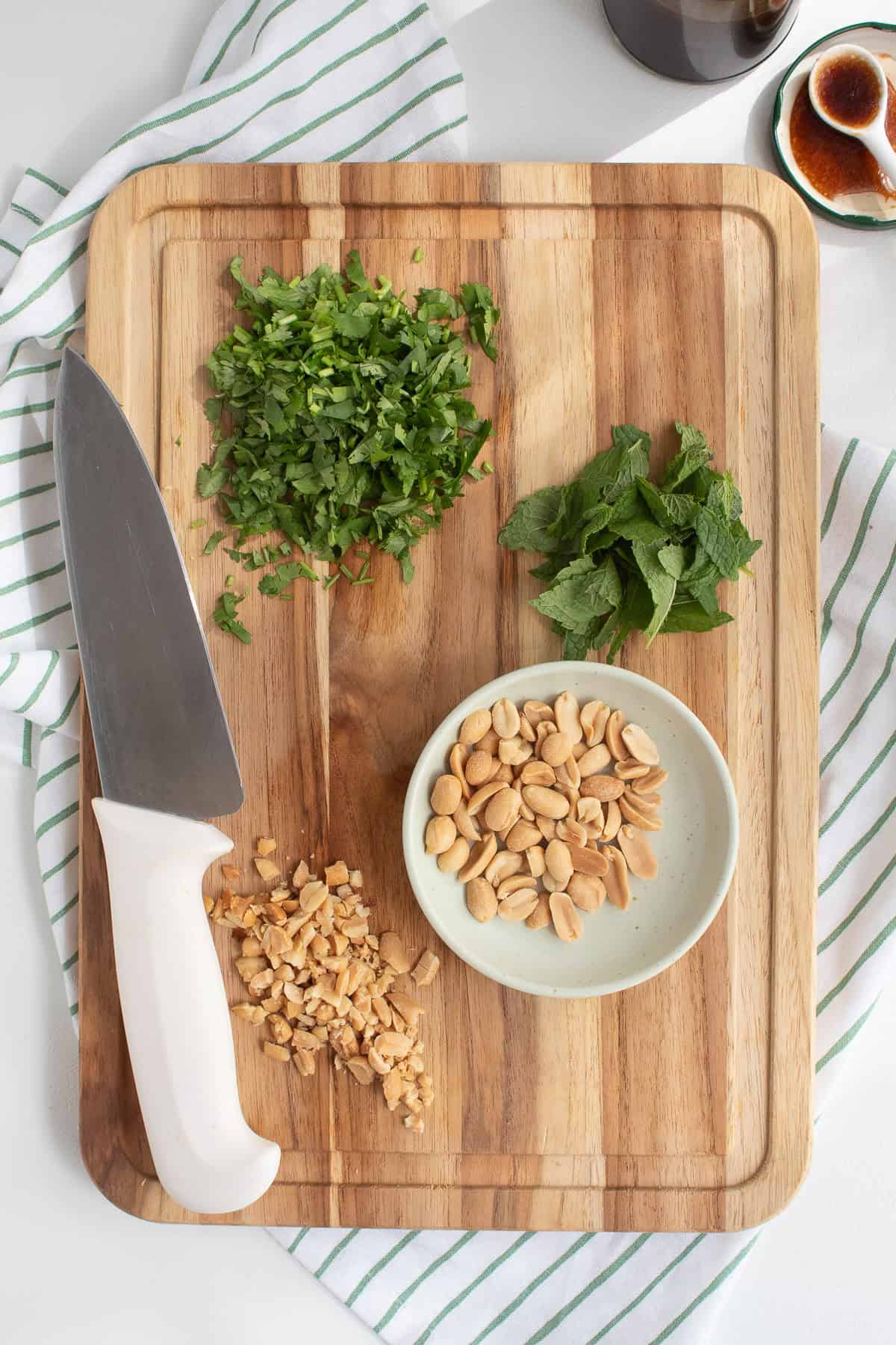 Cilantro, mint, and peanuts are prepared on a wooden cutting board.
