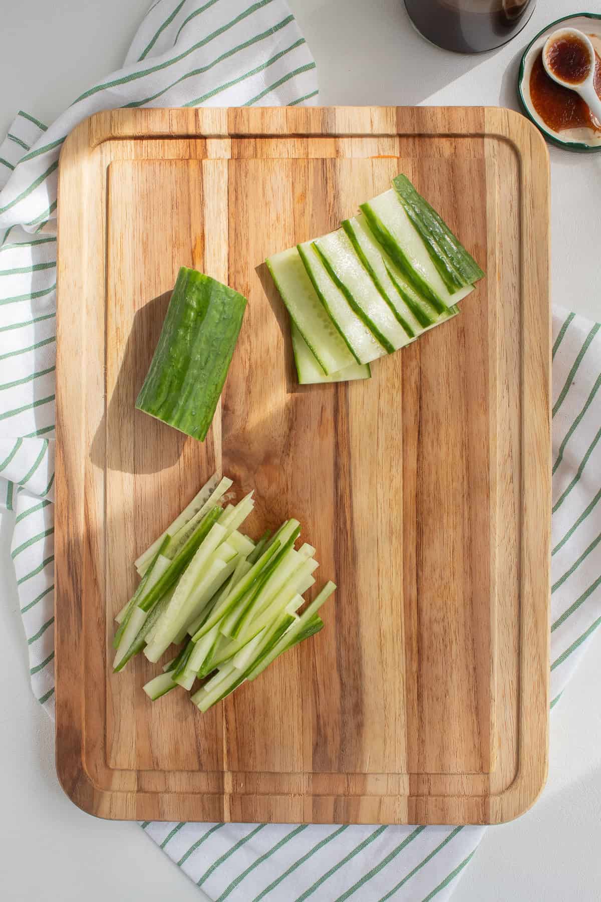 Cucumber strips are prepared on a wooden cutting board.