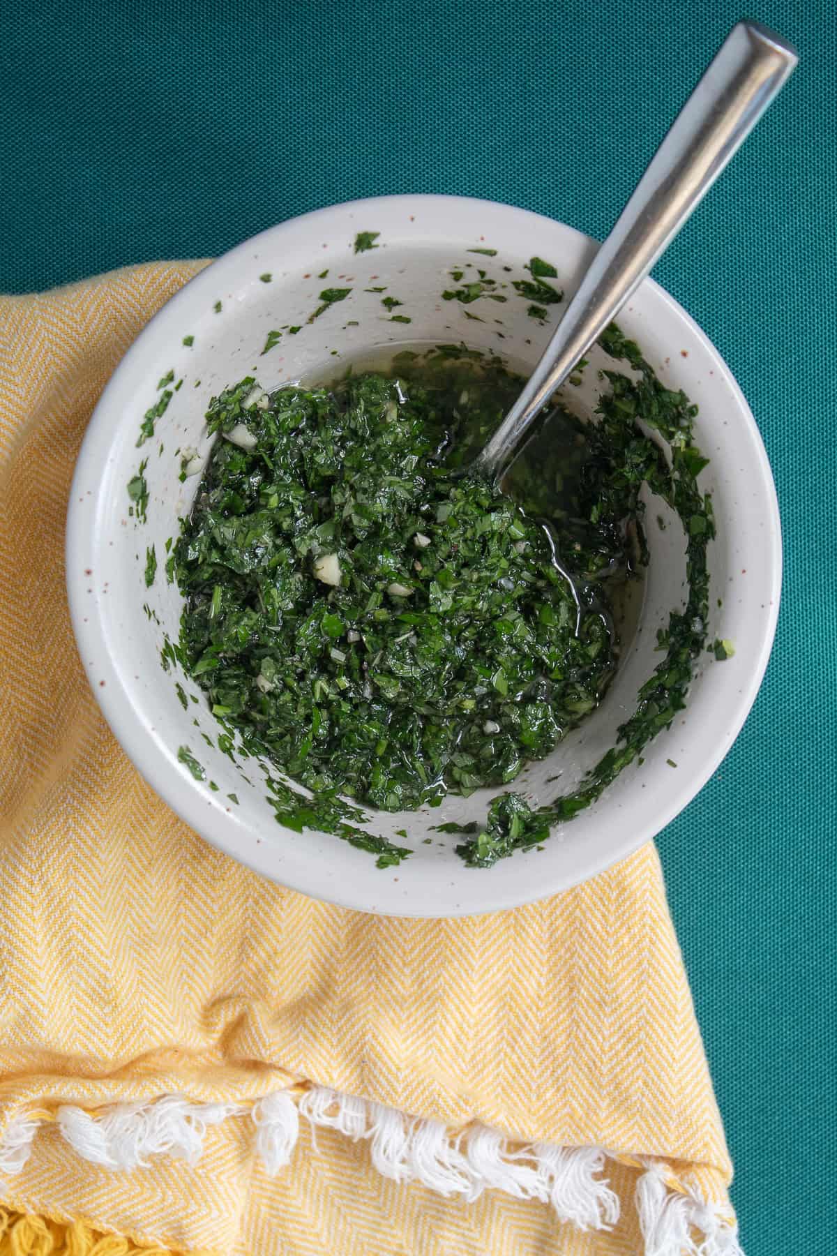 The deep green chimichurri sauce in a white bowl.