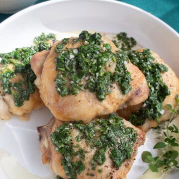 Chimichurri sauce is spooned over crisp roasted chicken thighs in a white bowl.