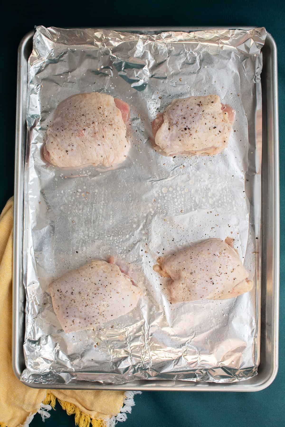 Chicken thighs are seasoned on a foil-lined pan.