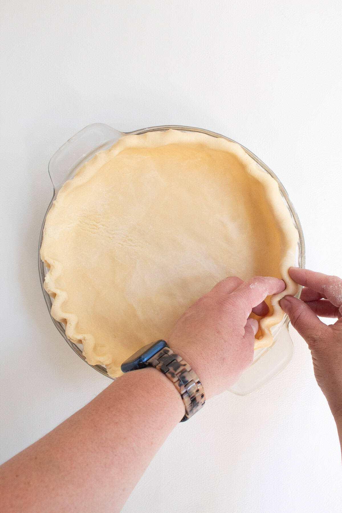 The edges of the pie crust are being crimped into a zig zag pattern using two hand.