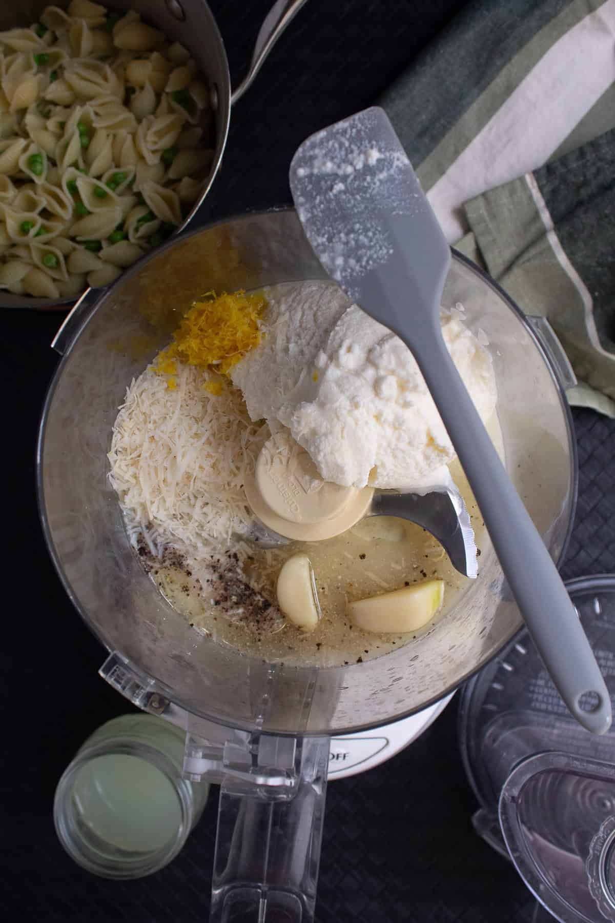 Ricotta, lemon juice and zest, Parmesan, salt, pepper, and garlic cloves are added to the food processor.