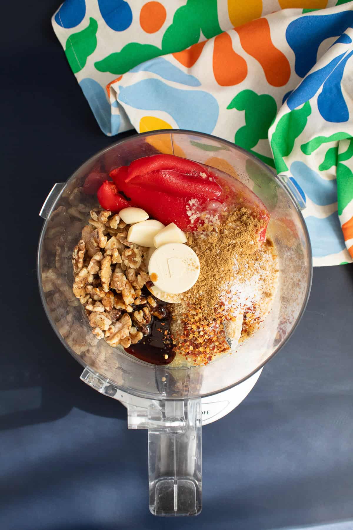 Garlic, roasted red peppers, walnuts, pomegranate molasses, chili flakes, lemon juice, and spices are added to a food processor.