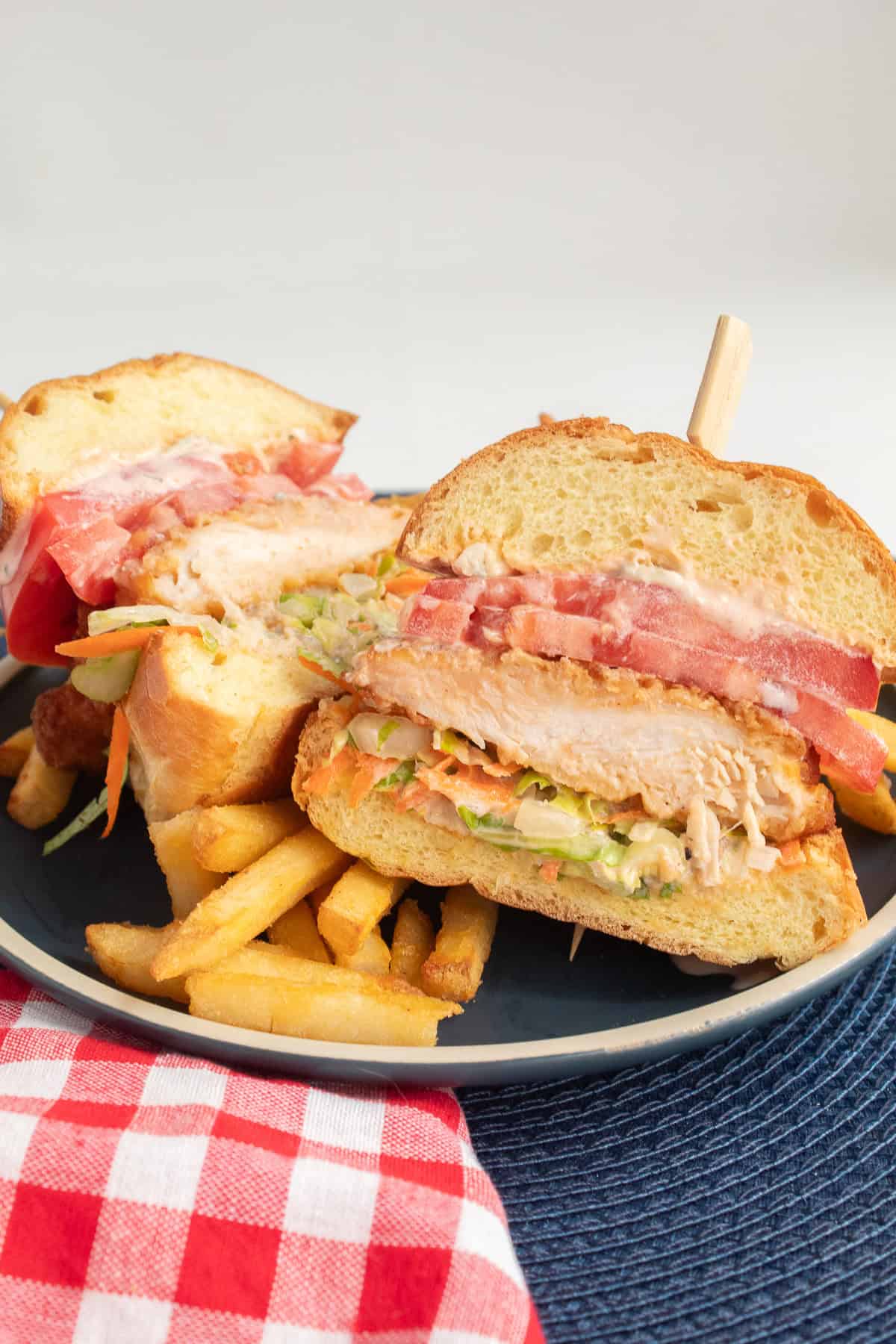 The buffalo chicken sandwich is cut in half, showing the layers of sauce, slaw, chicken breast, and tomato on the brioche bun.