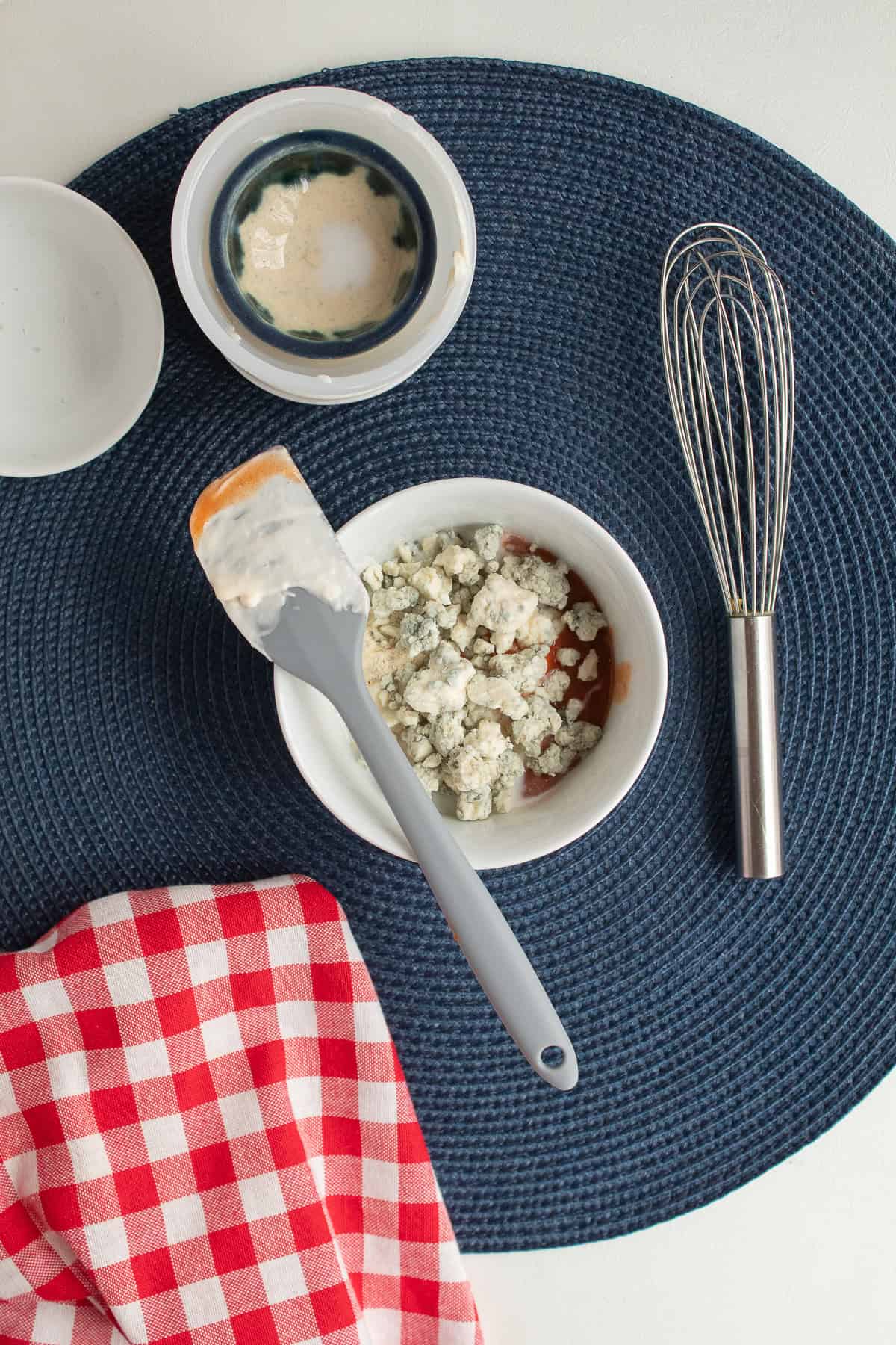 Crumbled blue cheese is combined with hot sauce in a white bowl for a tangy sandwich spread.