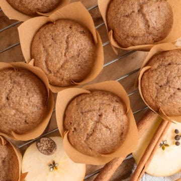 Baked applesauce muffins are golden brown in tulip muffin liners.