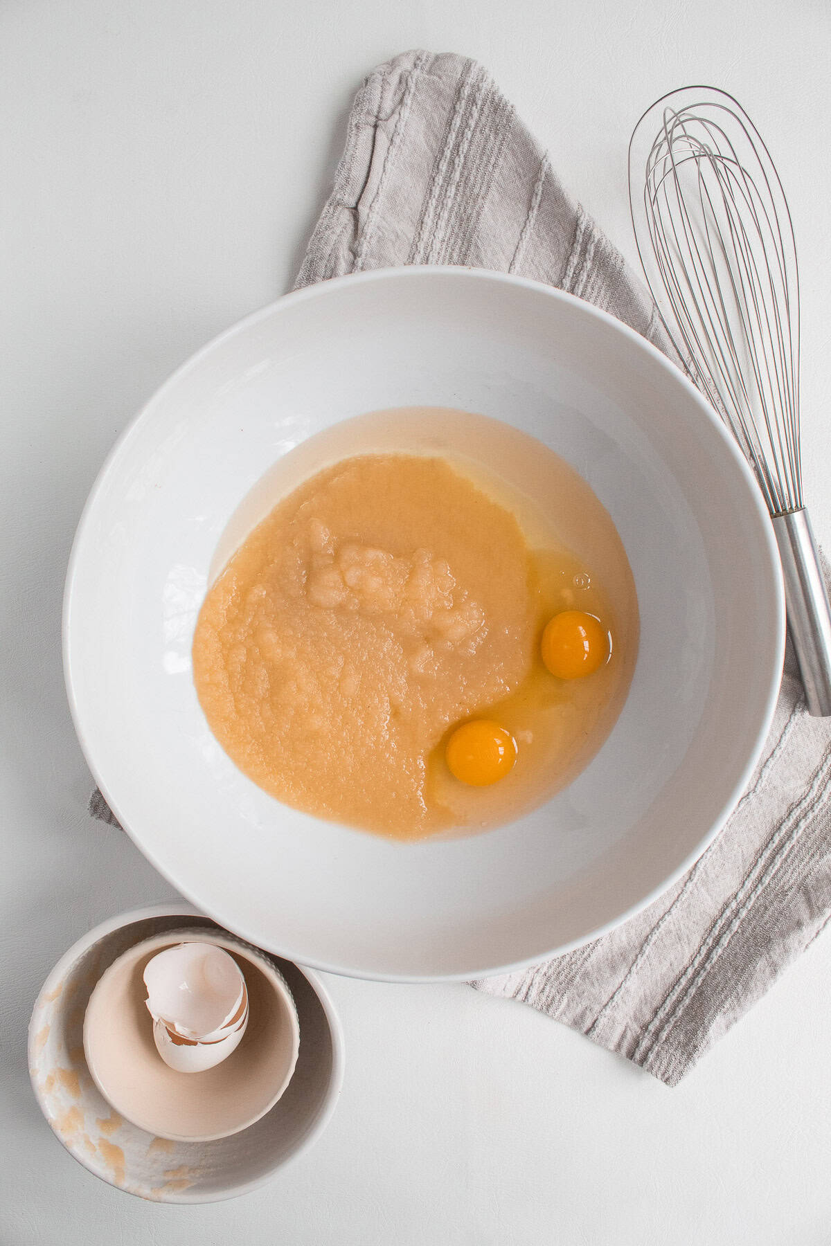 Eggs, oil, and applesauce are added to a large white bowl.