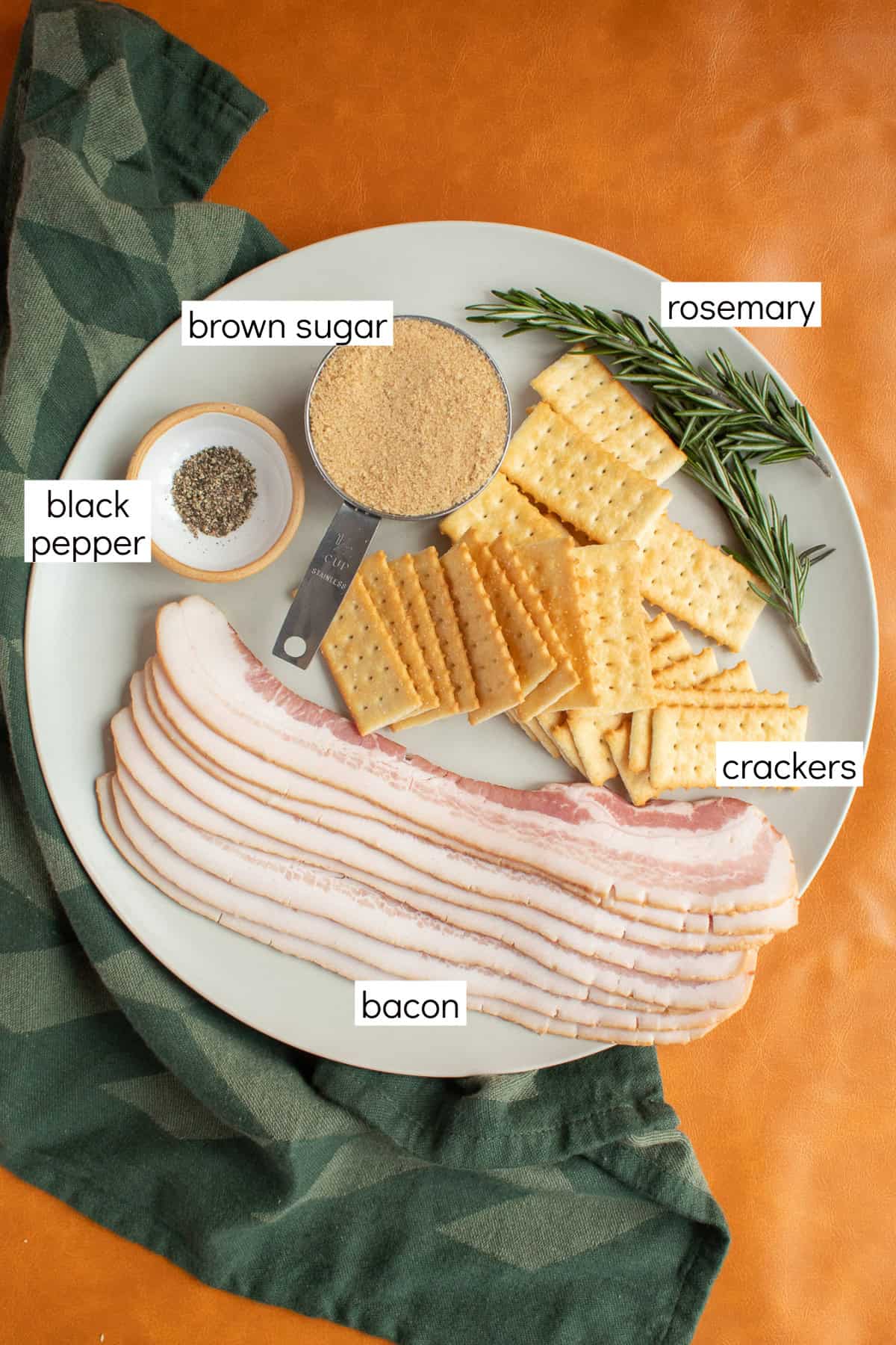Ingredients for the recipe are displayed and labeled with white text boxes including the words brown sugar, rosemary, crackers, bacon, and black pepper.