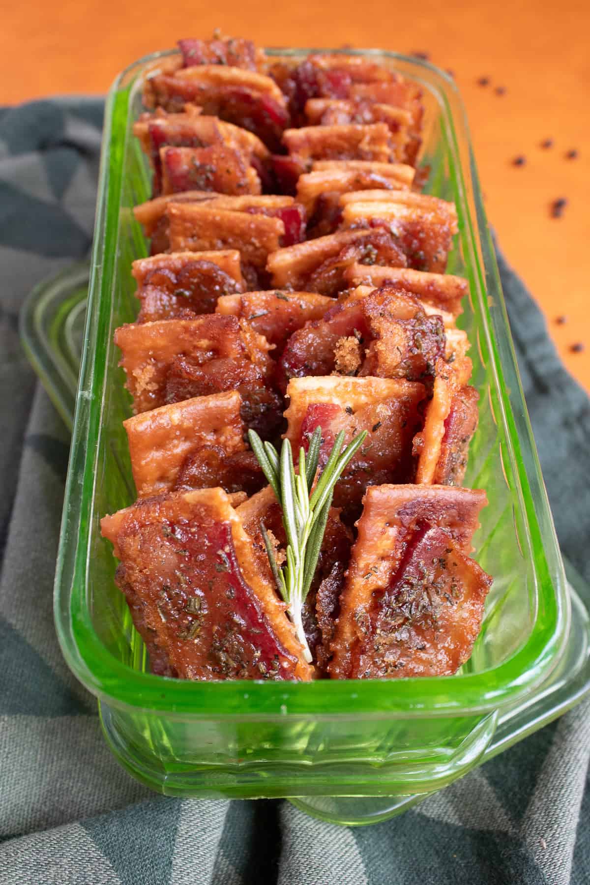Baked bacon crackers stacked in a green glass serving dish.