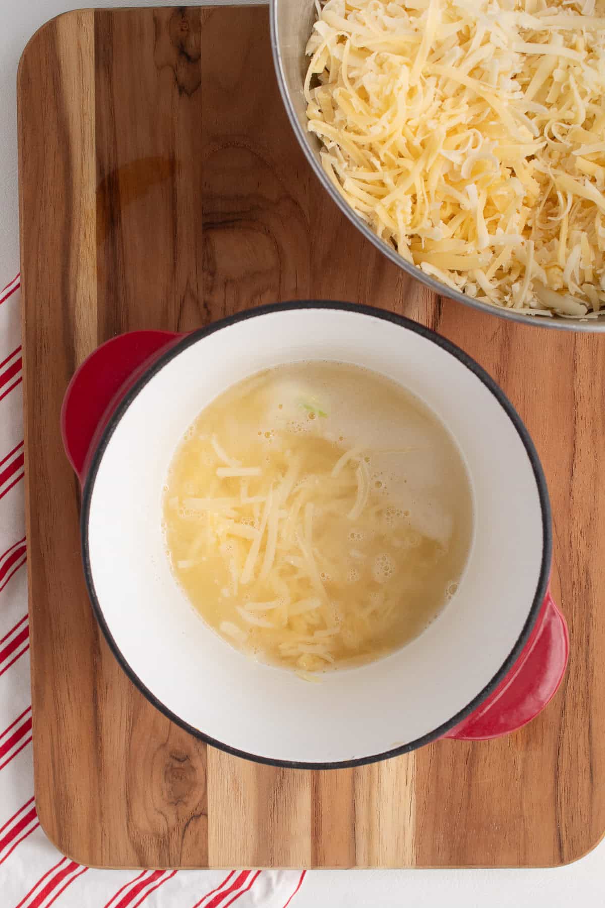 Shredded cheese is slowly added to the simmering wine mixture.