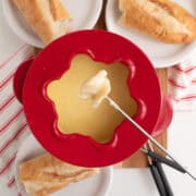 A piece of bread on a long fork is dipped in the cheese fondue.