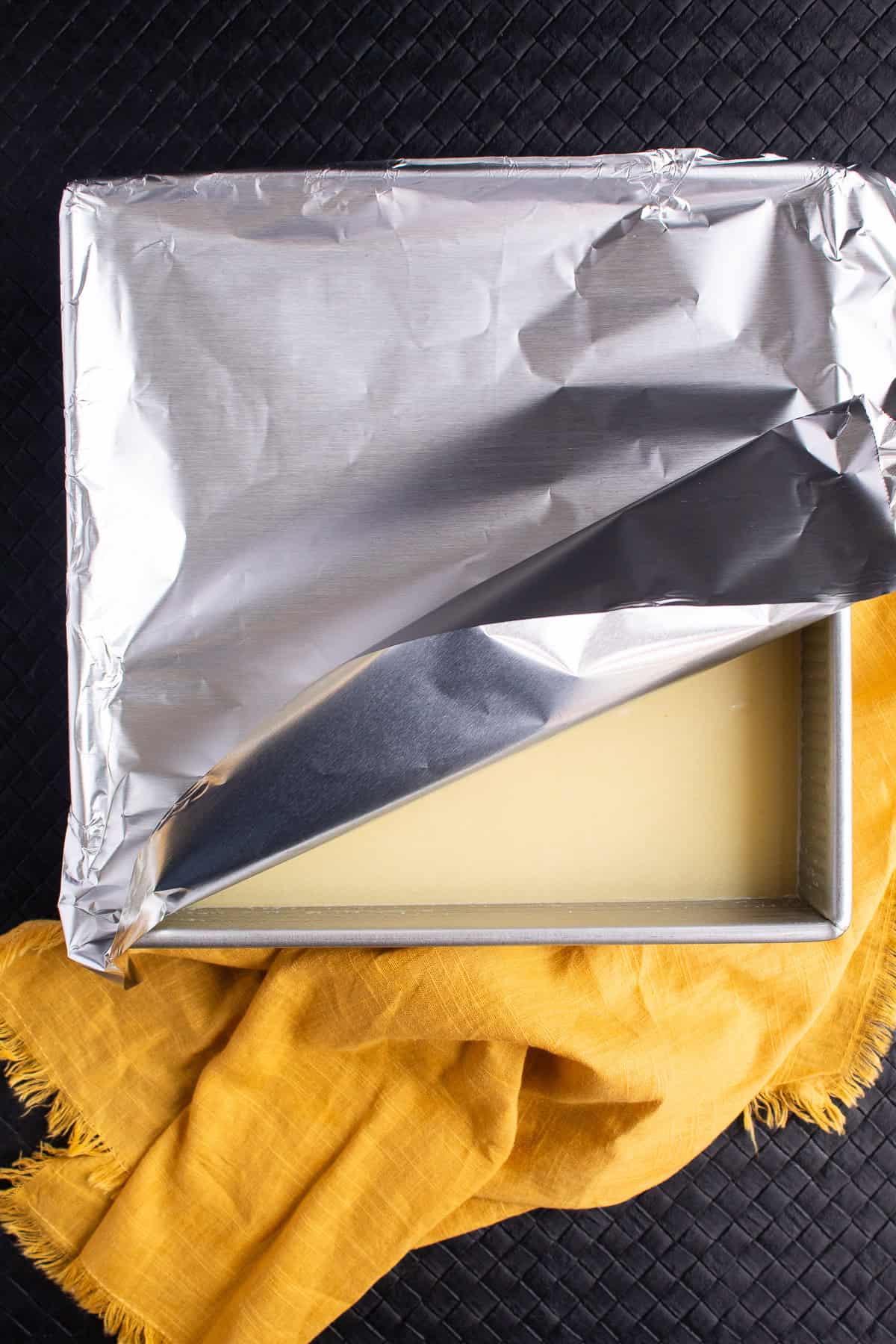 The rice and broth in the baking pan are tightly covered with foil before baking.