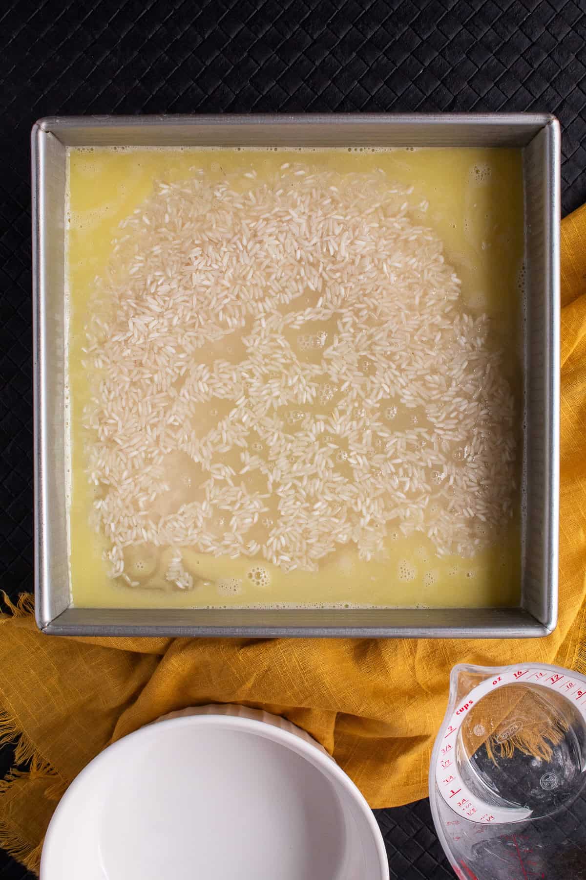The rice is added to the flavored broth in the baking pan.