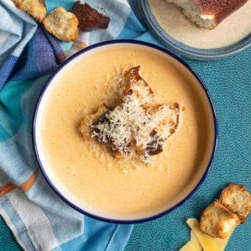 The creamy soup is displayed on a blue surface and is topped with pretzel bread croutons and additional shredded gouda cheese.