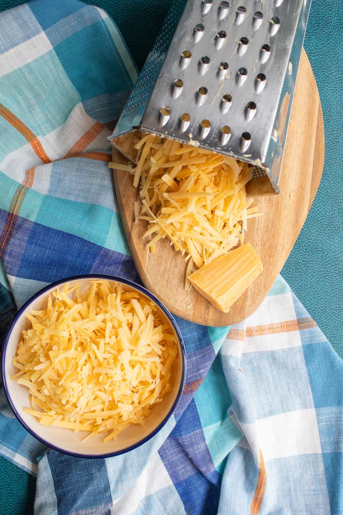 The gouda cheese is shredded on the large holes of a box grater.