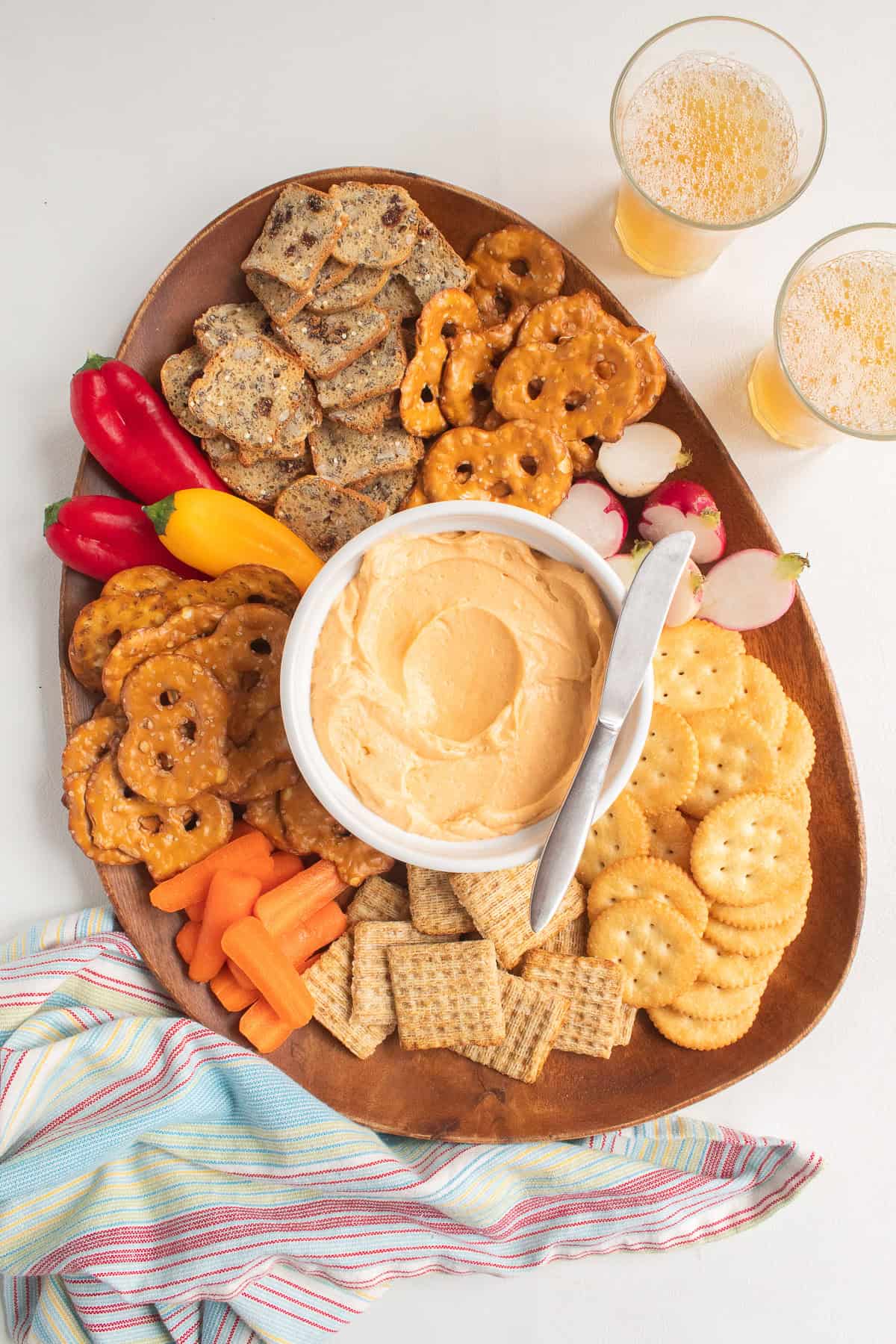 A party platter with vegetables, crackers, and chilled cheese spread is served with beer alongside.