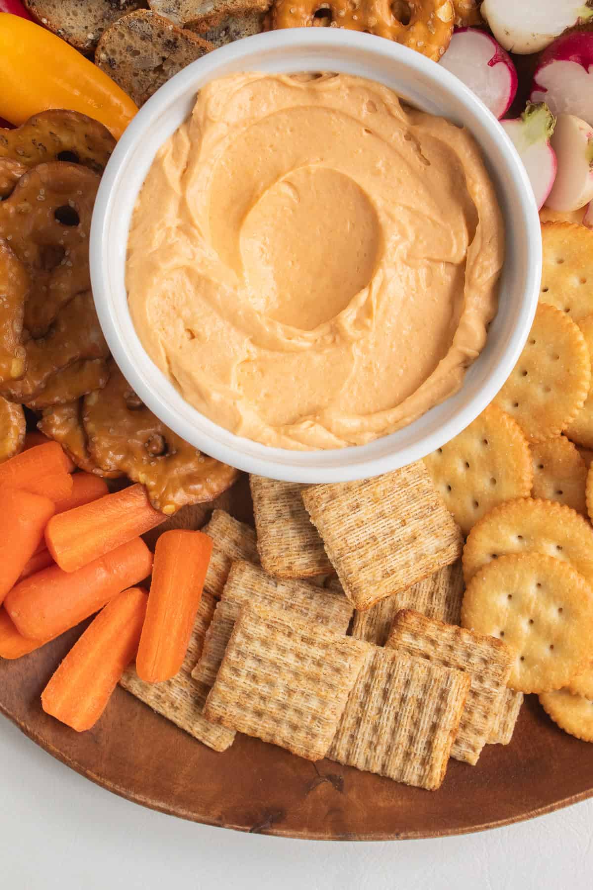 The chilled cheese spread is served with vegetables and crackers on a wood platter.