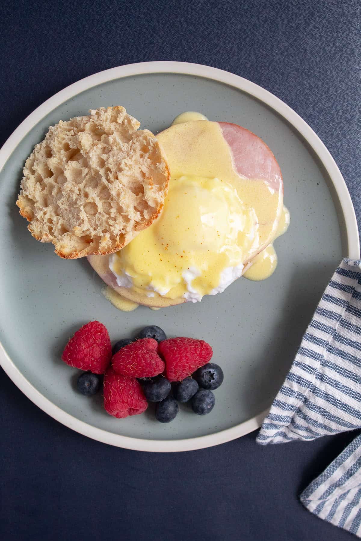 Hollandaise sauce is spooned over poached egg and ham on an english muffin for eggs benedict.