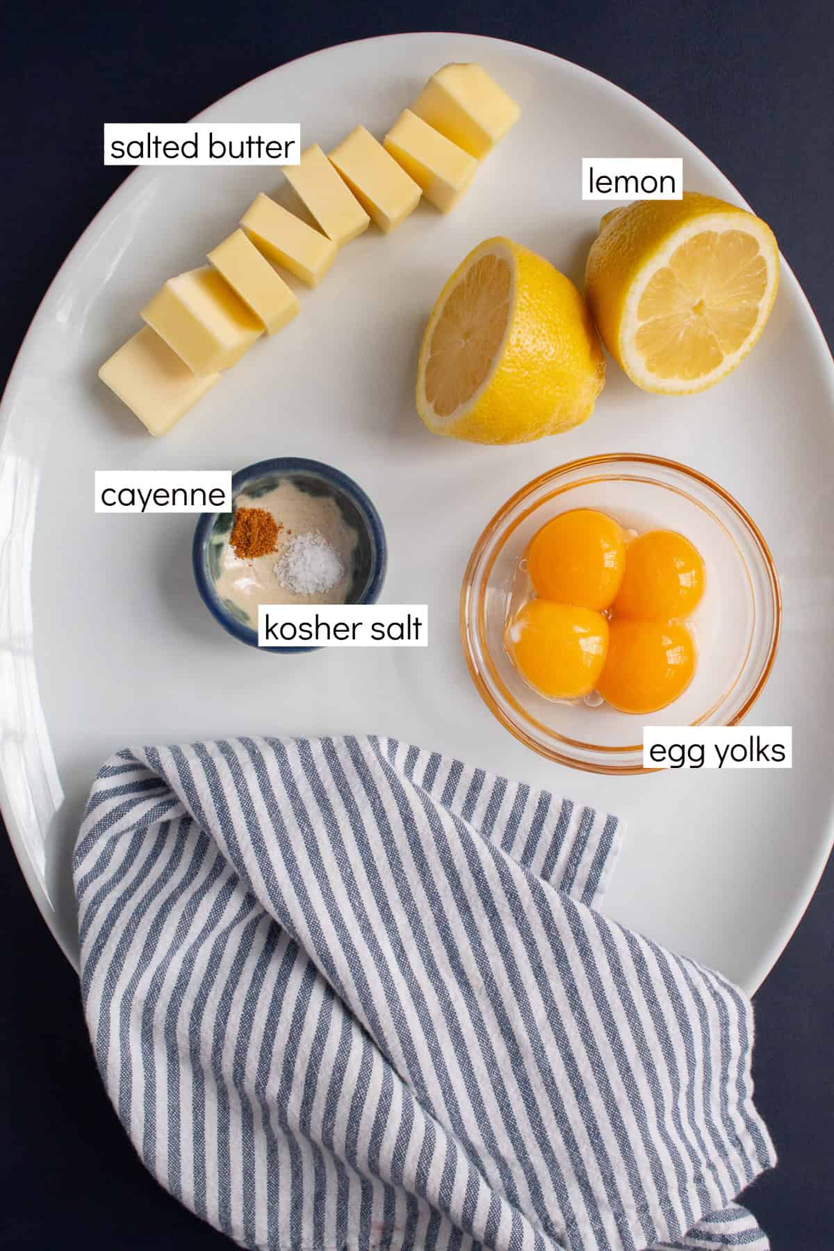 Ingredients for the recipe are displayed and labeled with white text boxes including the words salted butter, lemon, cayenne, kosher salt, and egg yolks.