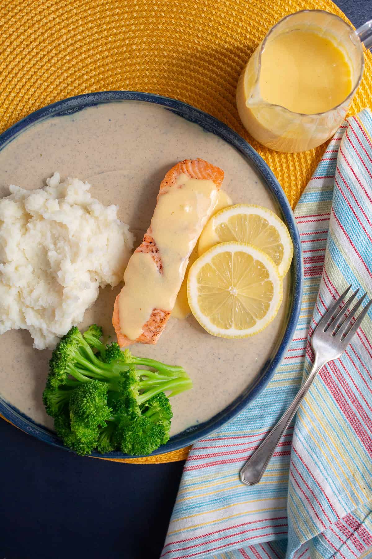 Hollandaise sauce drizzled over a salmon filet on a plate with steamed broccoli and mashed potatoes.