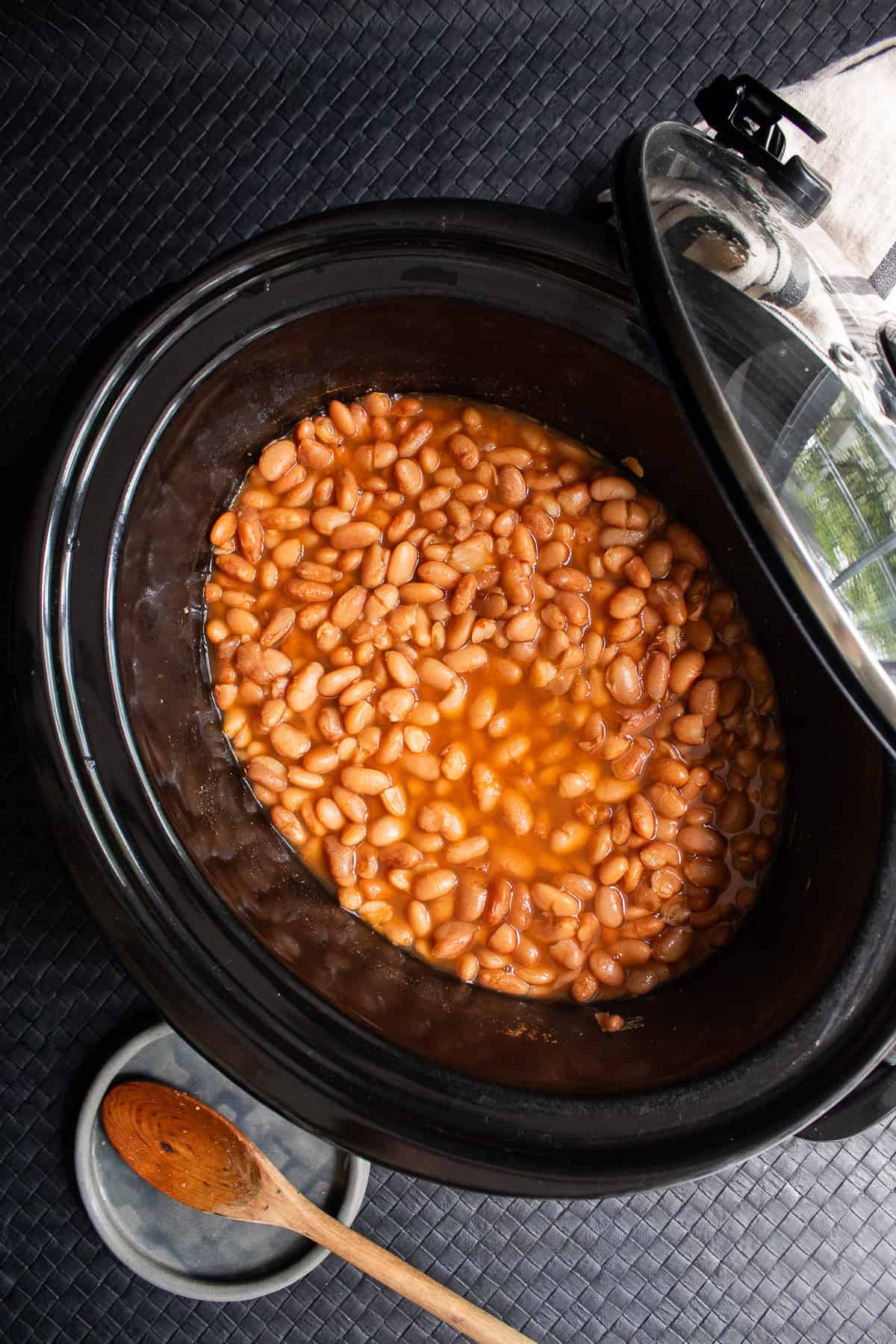 Brothy cooked beans sit in the bottom of a large slow cooker.