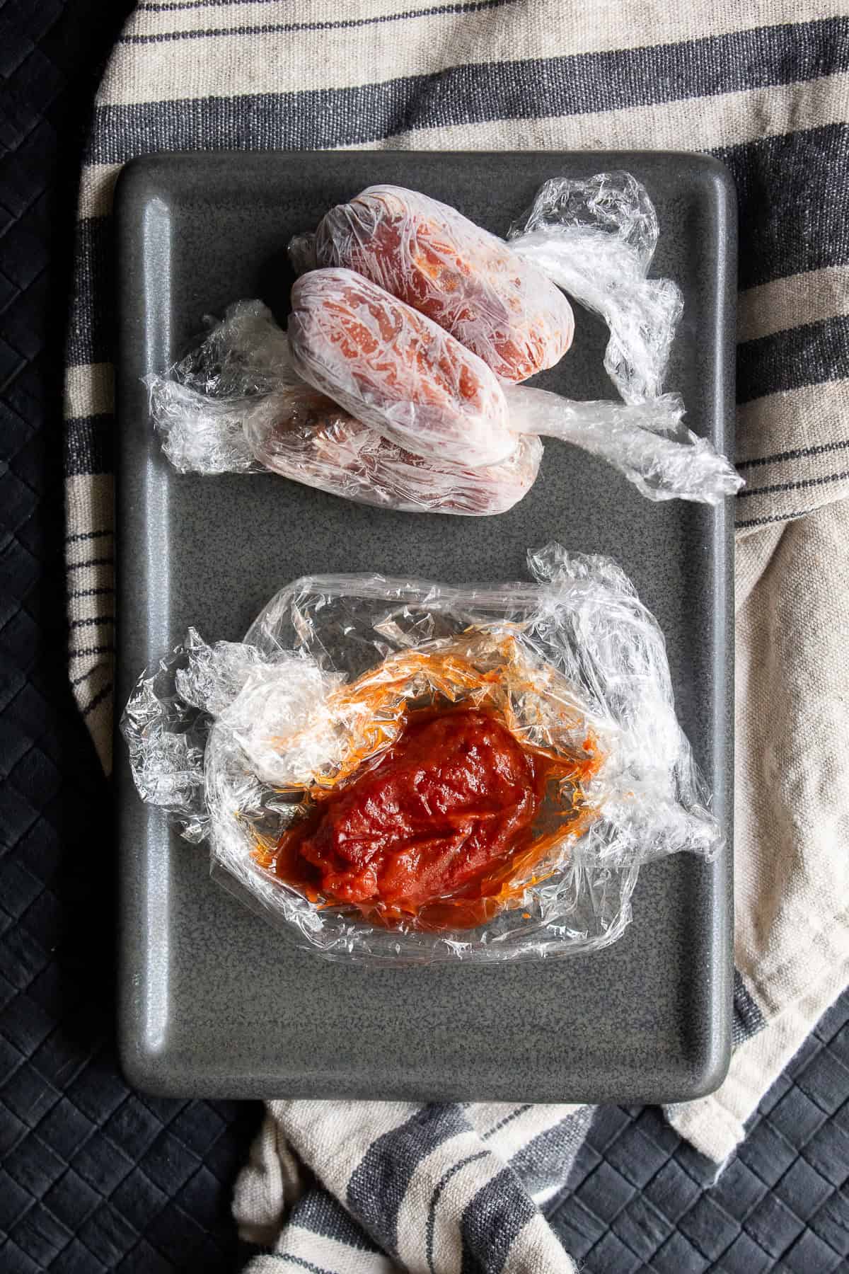 A chipotle in adobo sauce is in a nest of plastic wrap near other frozen parcels of chipotle peppers.