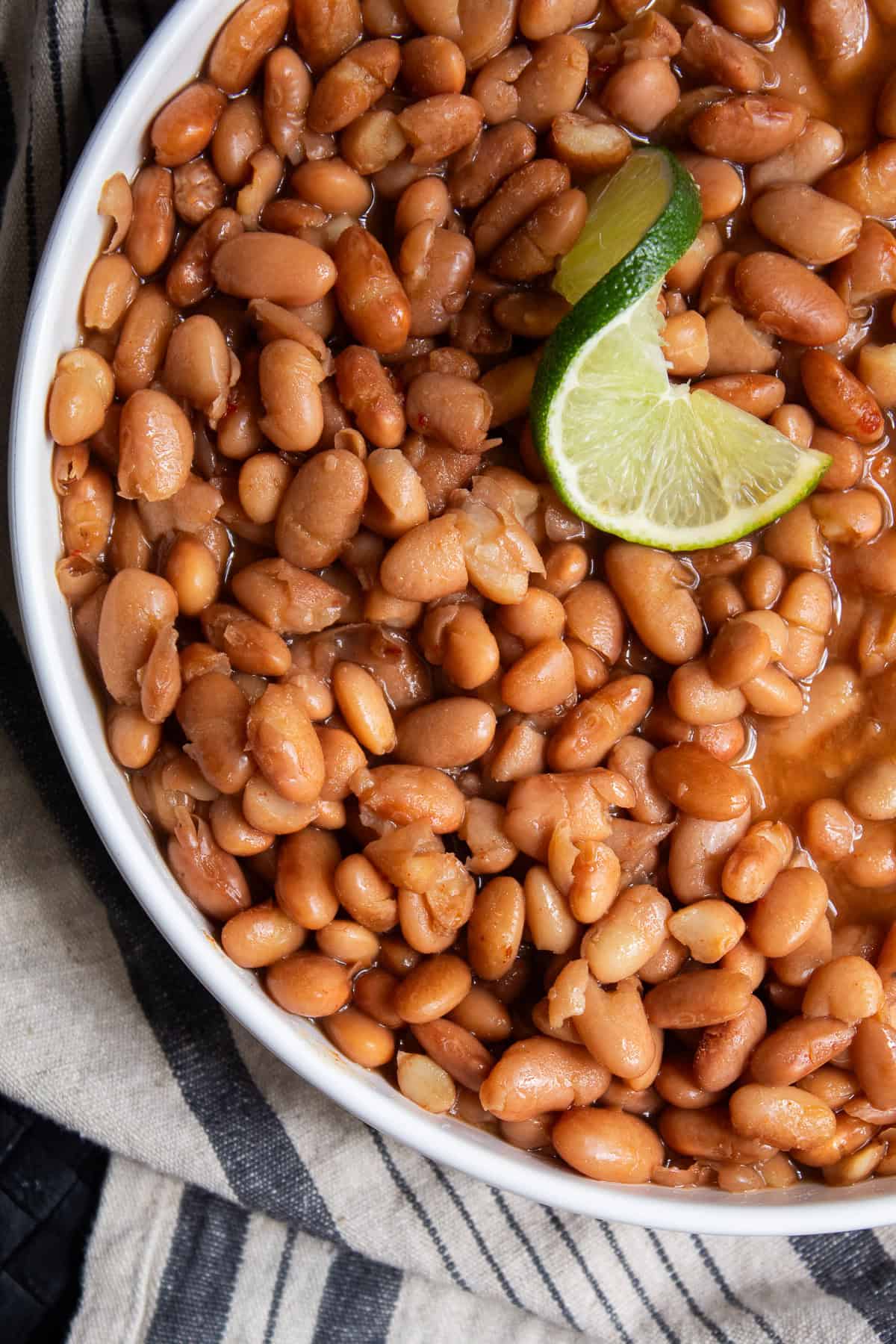 A white platter is filled with cooked pinto beans and garnished with lime.