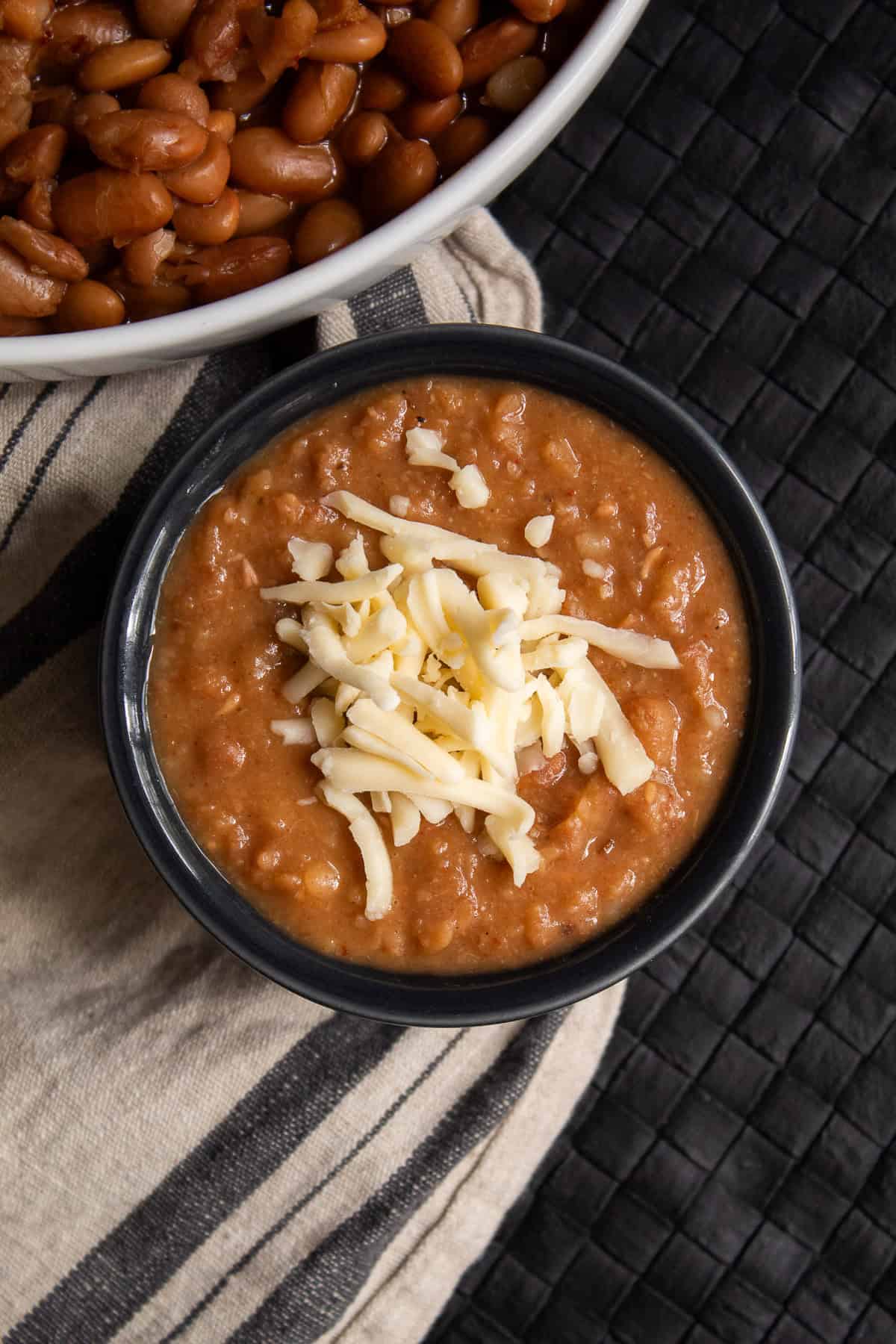 Pinto beans are mashed and garnished with shredded cheese in a gray bowl.