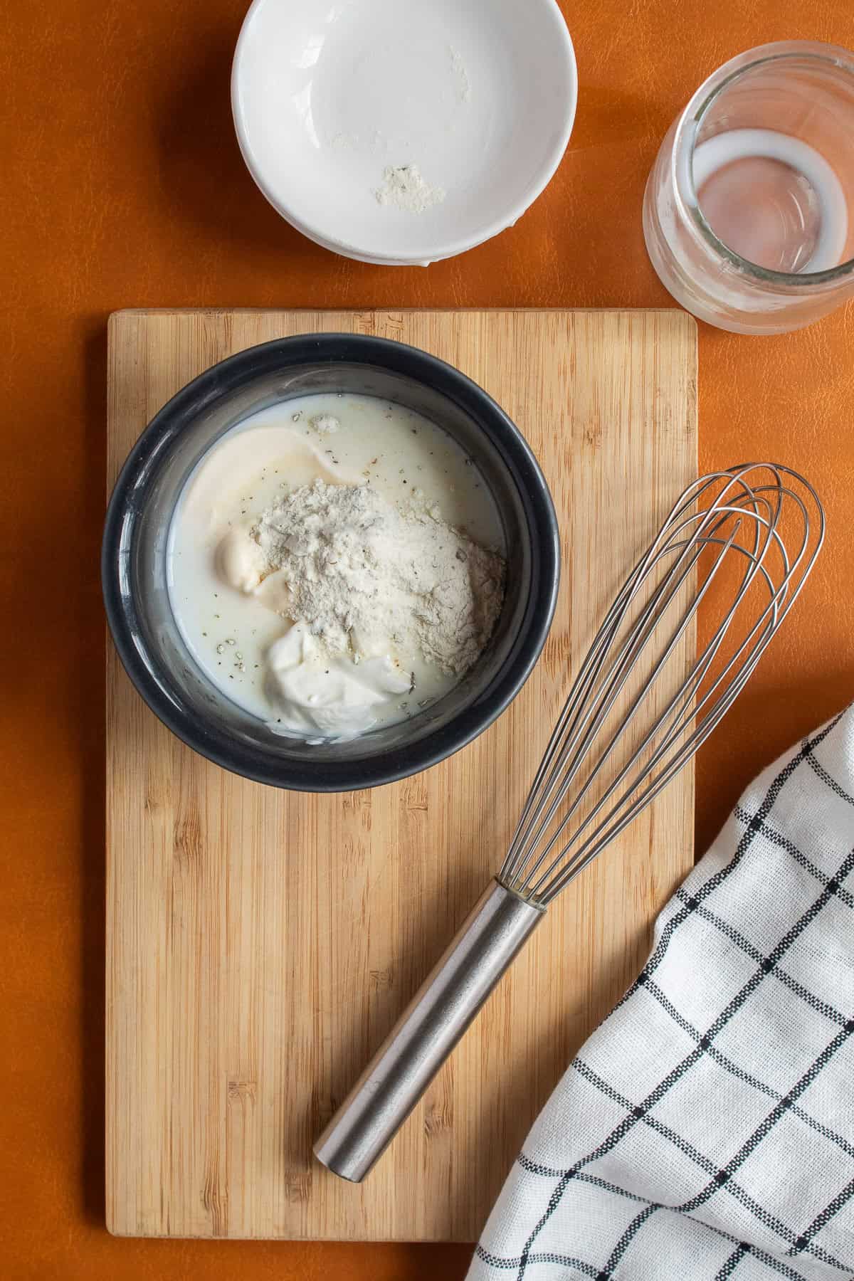 Milk, sour cream, mayonnaise, and ranch dressing mix are added to a small gray bowl.