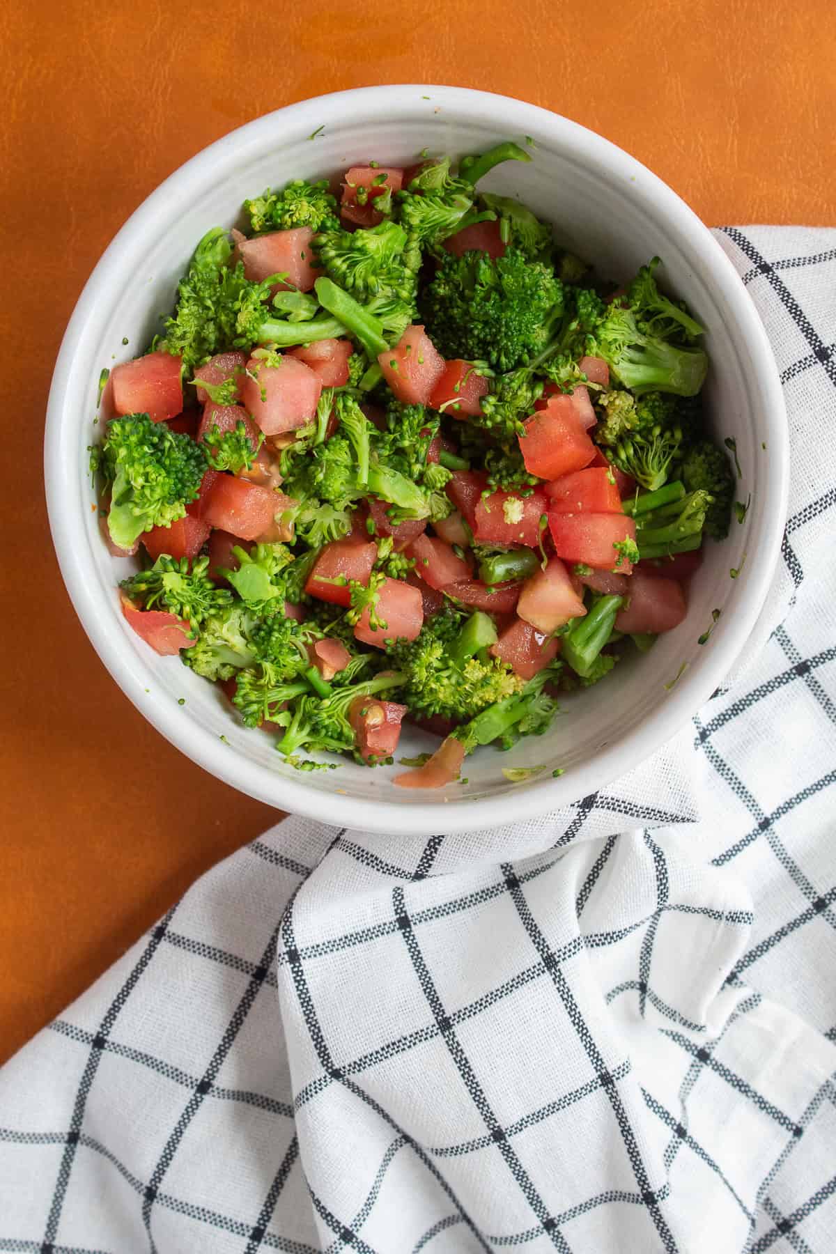 Finely chopped steamed broccoli and diced tomato mixed together in a bowl.
